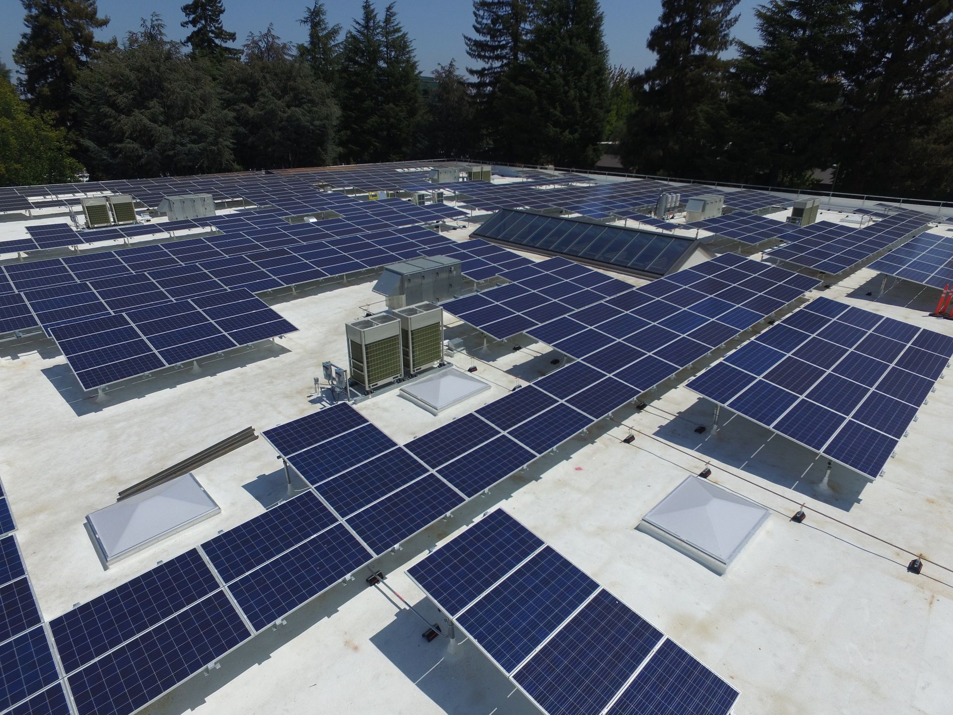 A high-angle view of a flat commercial building roof covered in a large grid of dark blue solar panels.