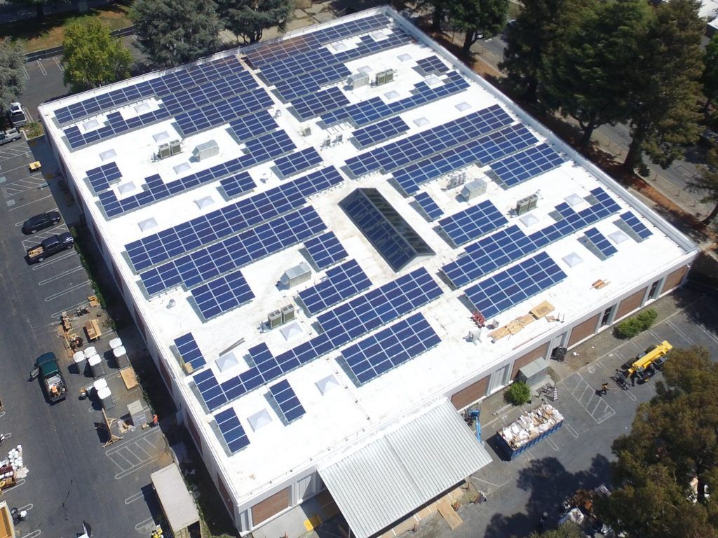 Aerial view of a flat building roof completely covered in dark solar panel arrays.