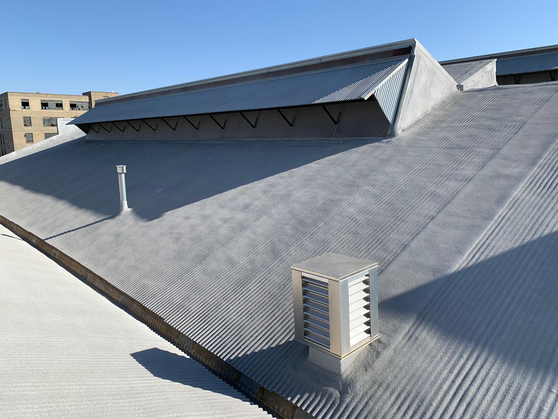 A slanted, corrugated gray metal roof featuring a ridge vent, a small exhaust chimney, and a square ventilation unit.