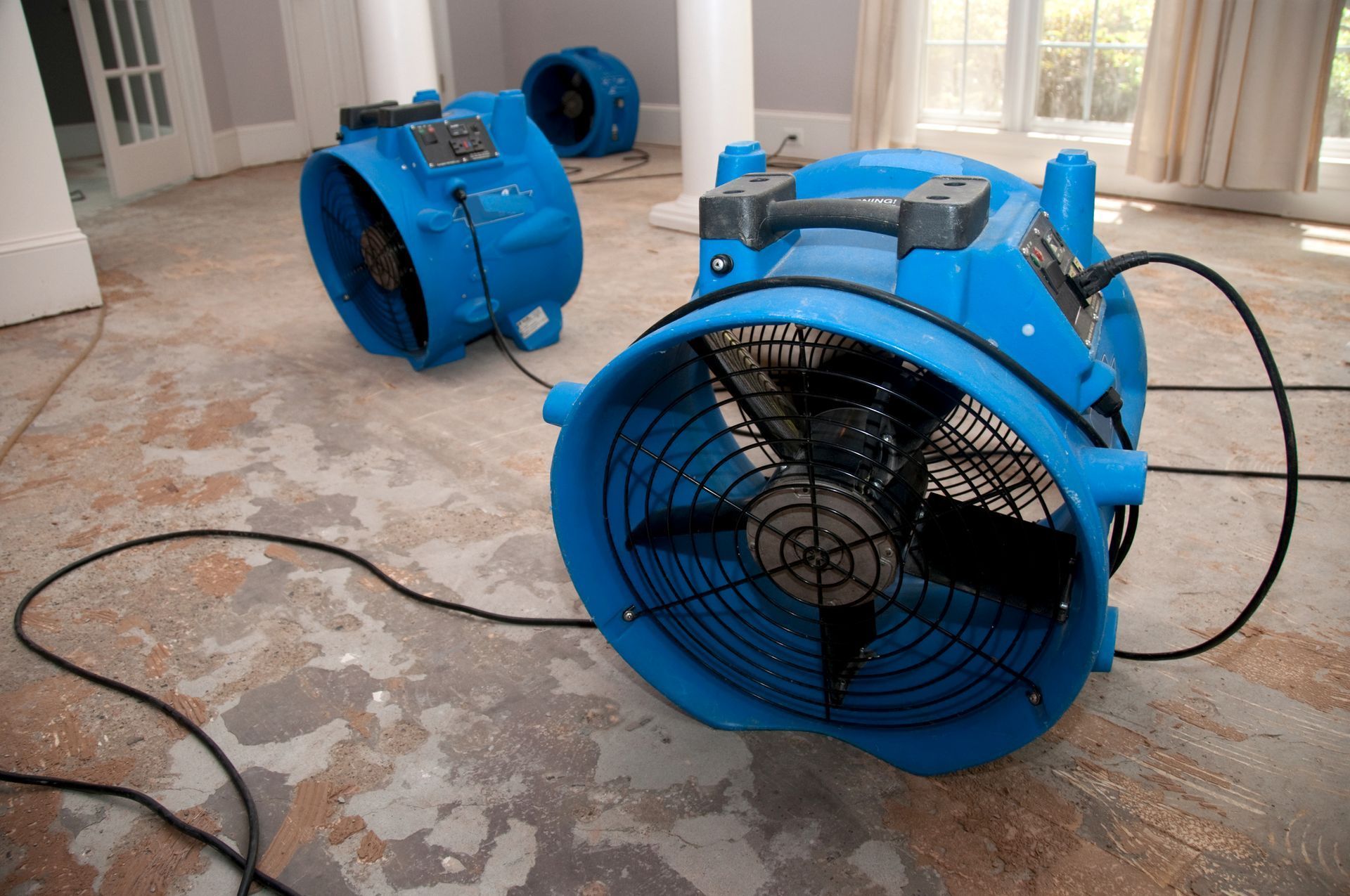 Three blue industrial floor fans placed on a damaged indoor floor, indicating professional water damage restoration.