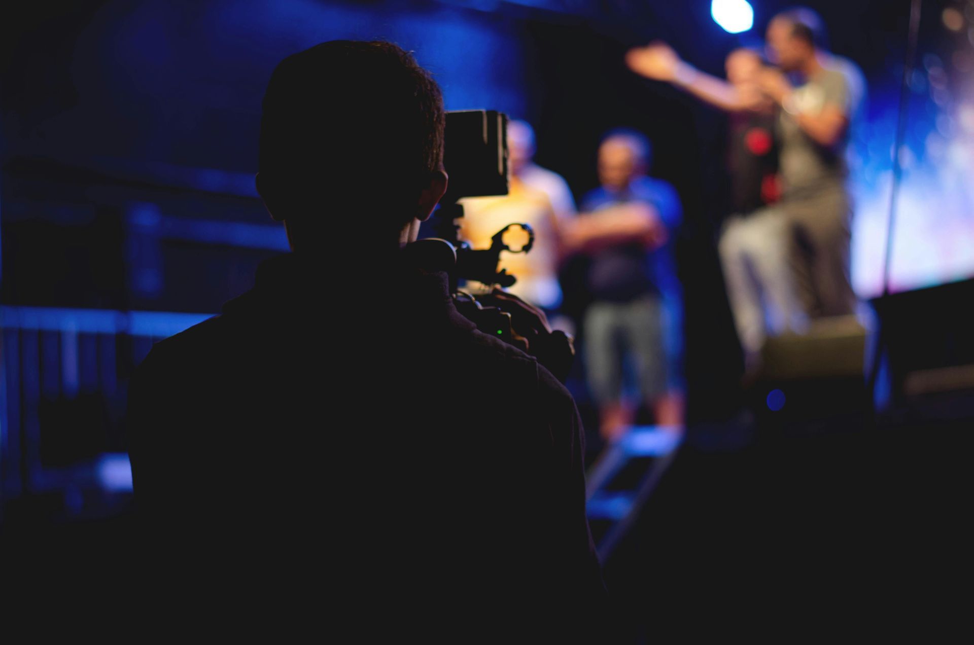 A man is holding a camera in front of a group of people on a stage.
