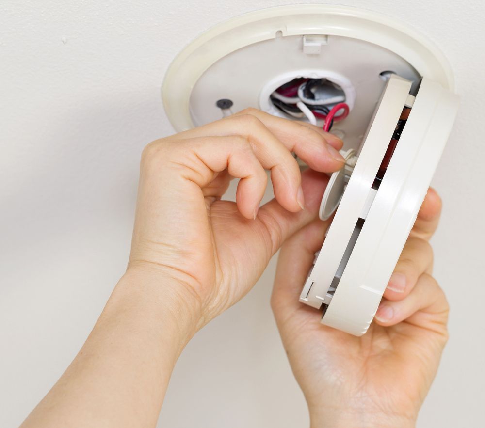 Hands Installing a White Smoke Detector on a Ceiling, Wiring Visible — White Rose Electrical in Coffs Harbour, NSW