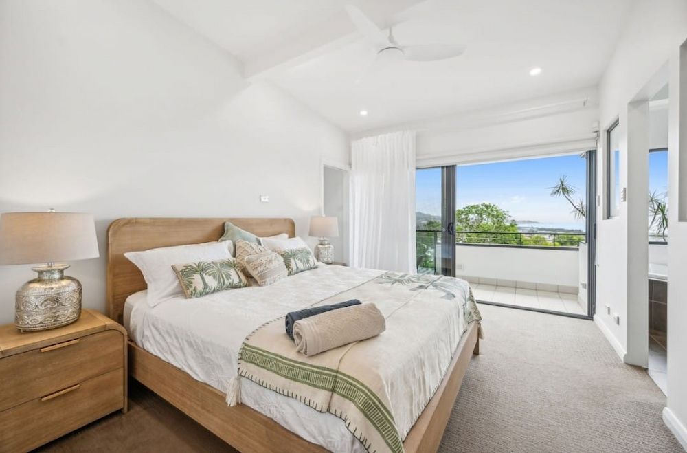 Bedroom With a Wooden Bed, Nightstand, and Balcony — White Rose Electrical in Coffs Harbour, NSW