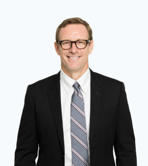 A man in a suit and black shirt is standing with his hands in his pockets.