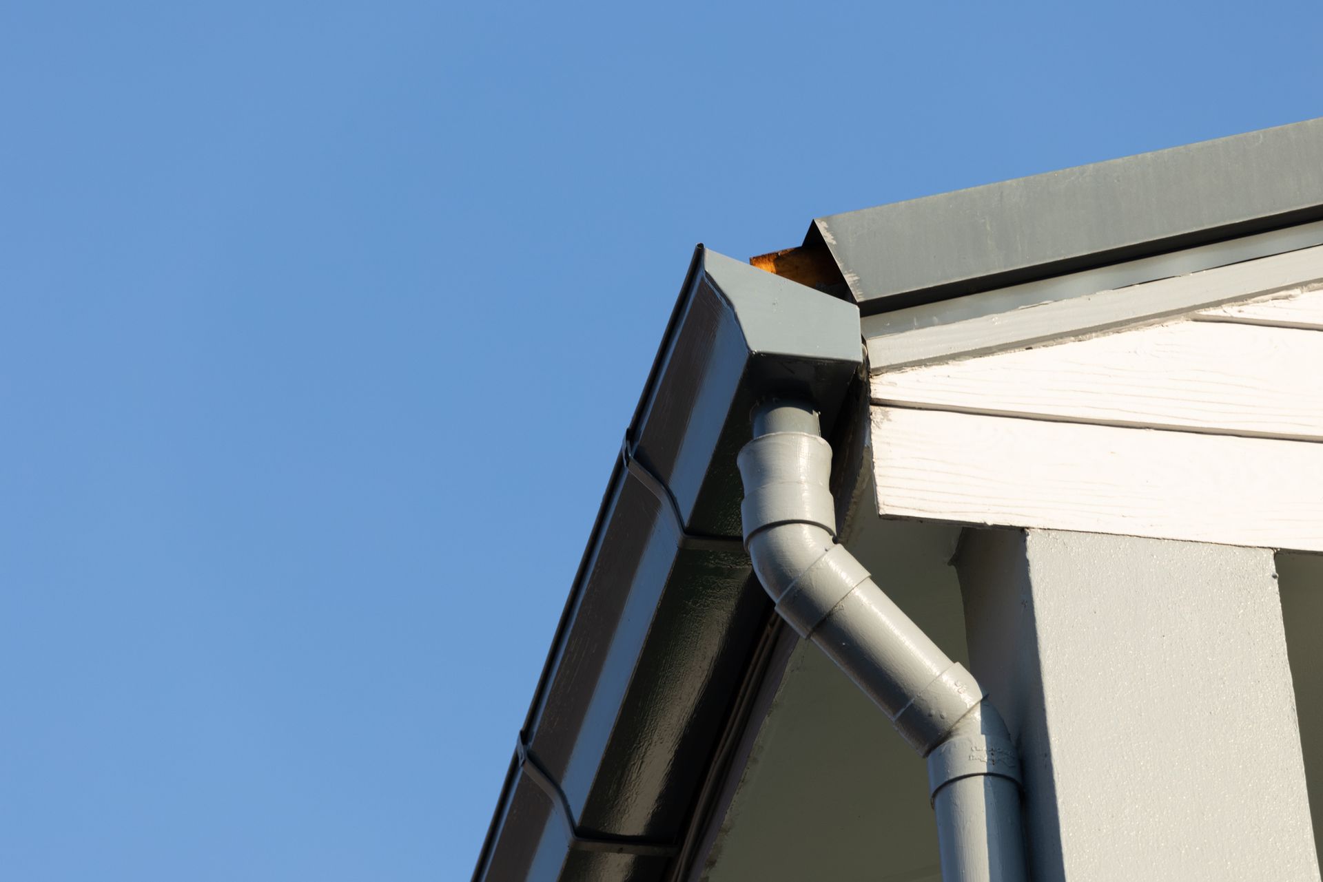 Gutter downspout at roof corner under a clear blue sky.