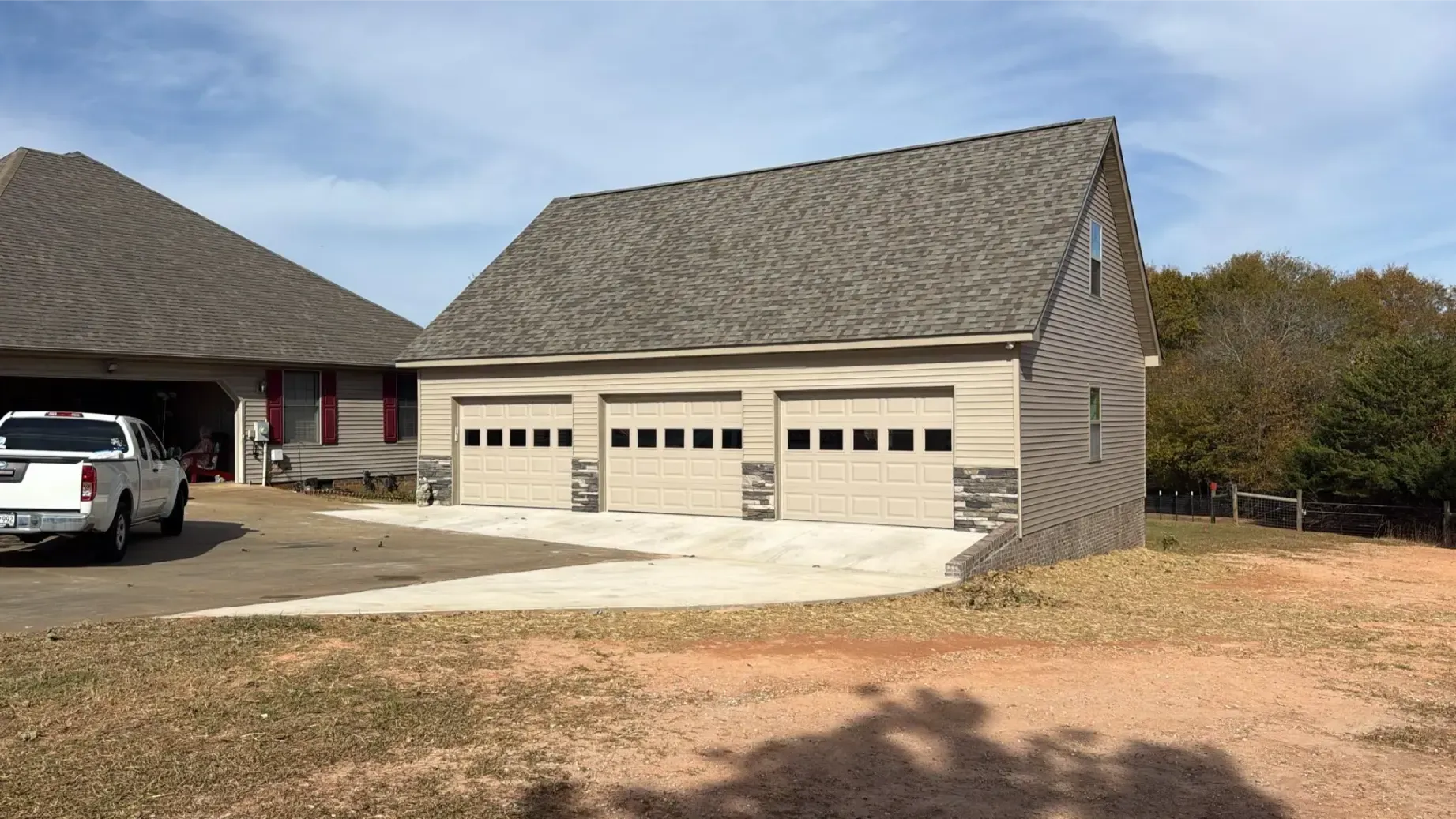 Two-car gray garage with white doors, surrounded by green trees. Two white chairs sit on a green lawn.