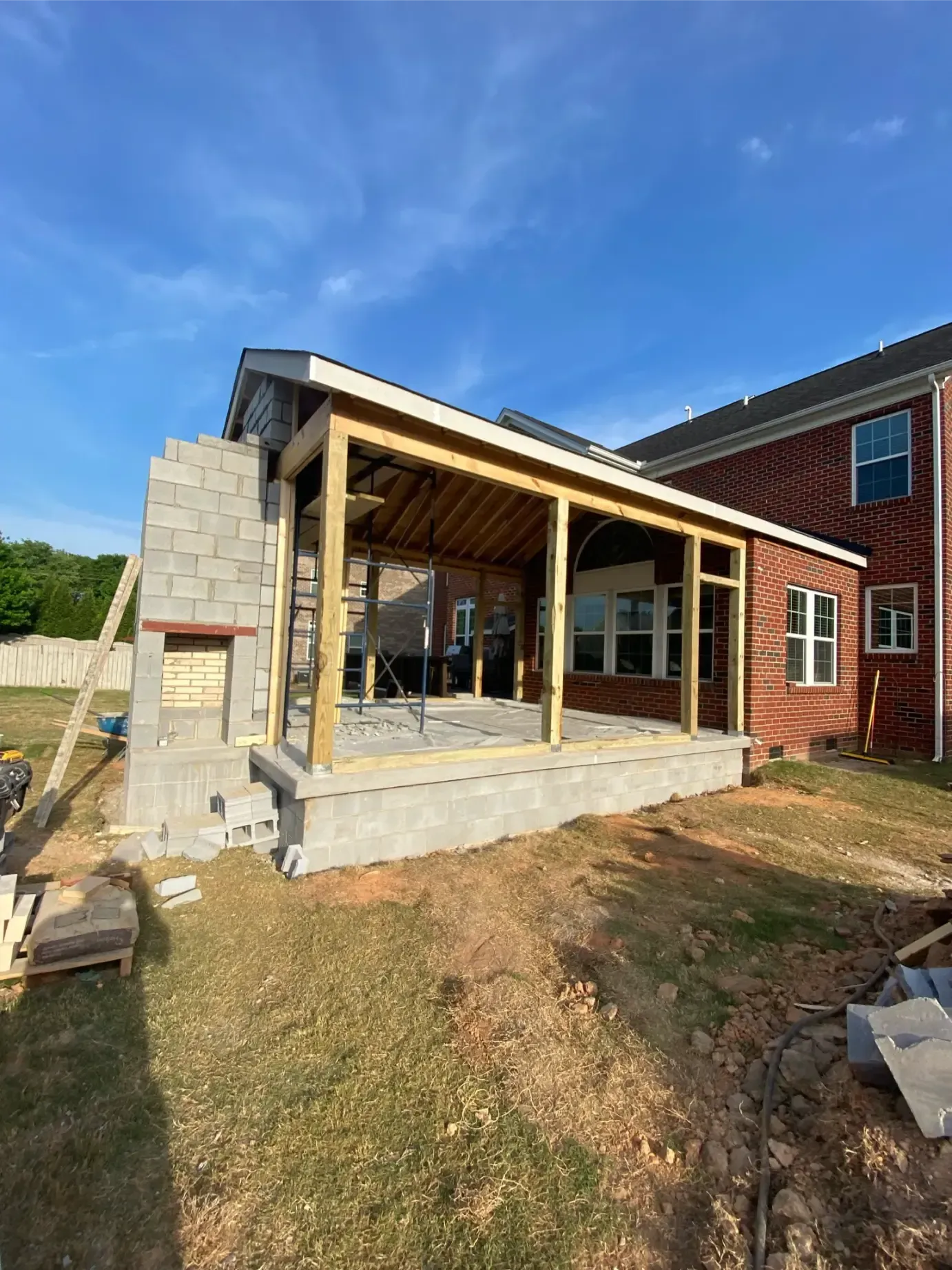 Exterior view of a brick house under renovation. A worker on a ladder is inside a new addition.
