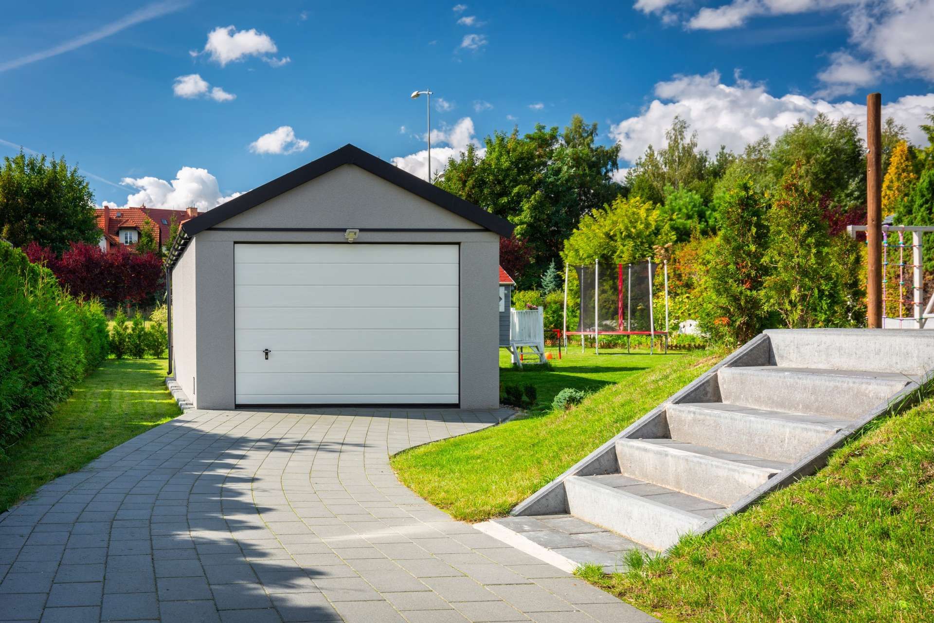 Gray garage with a white door, a paved driveway, and stone steps leading up a grassy hill.