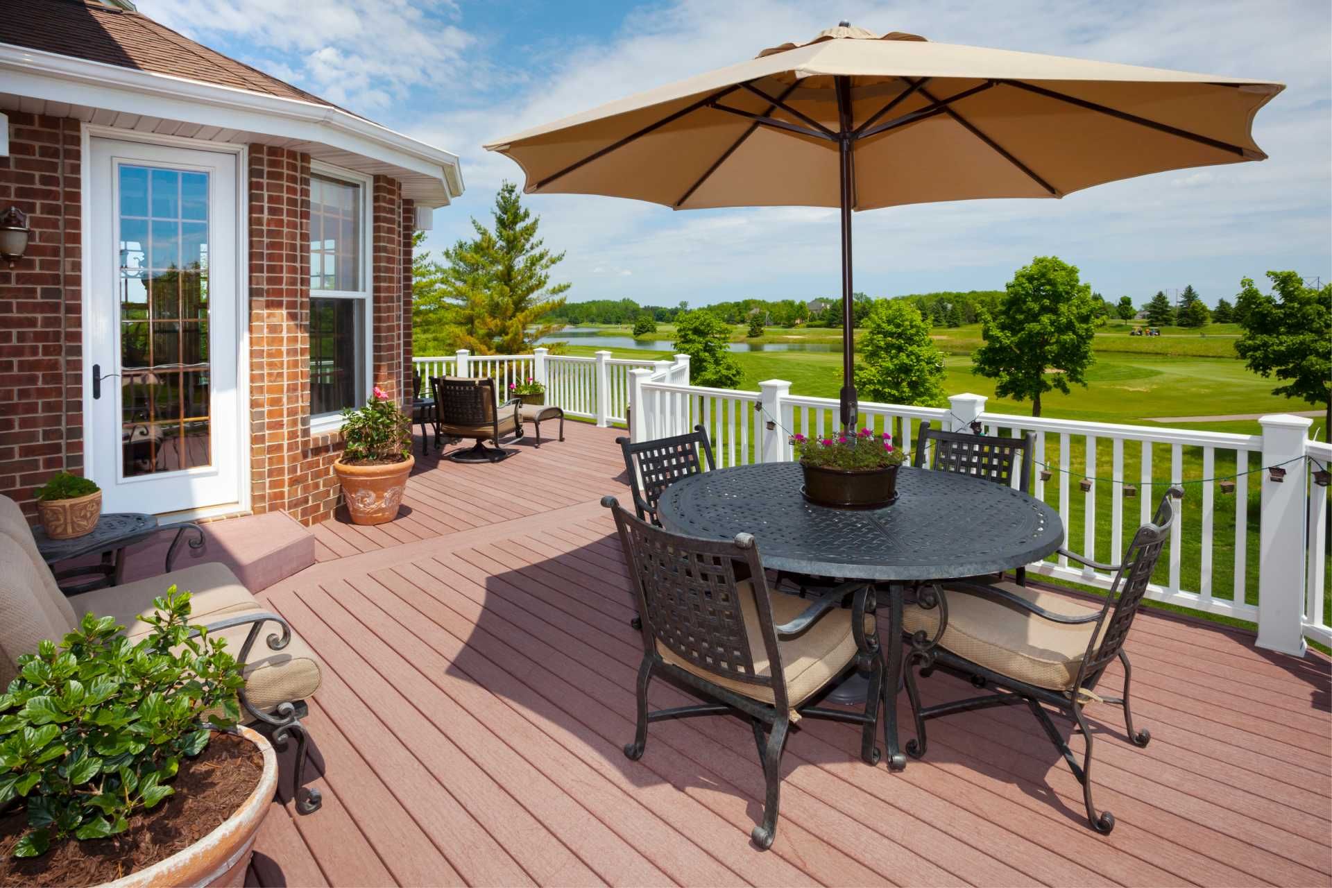 Wooden deck with patio furniture, umbrella, and golf course view on a sunny day.