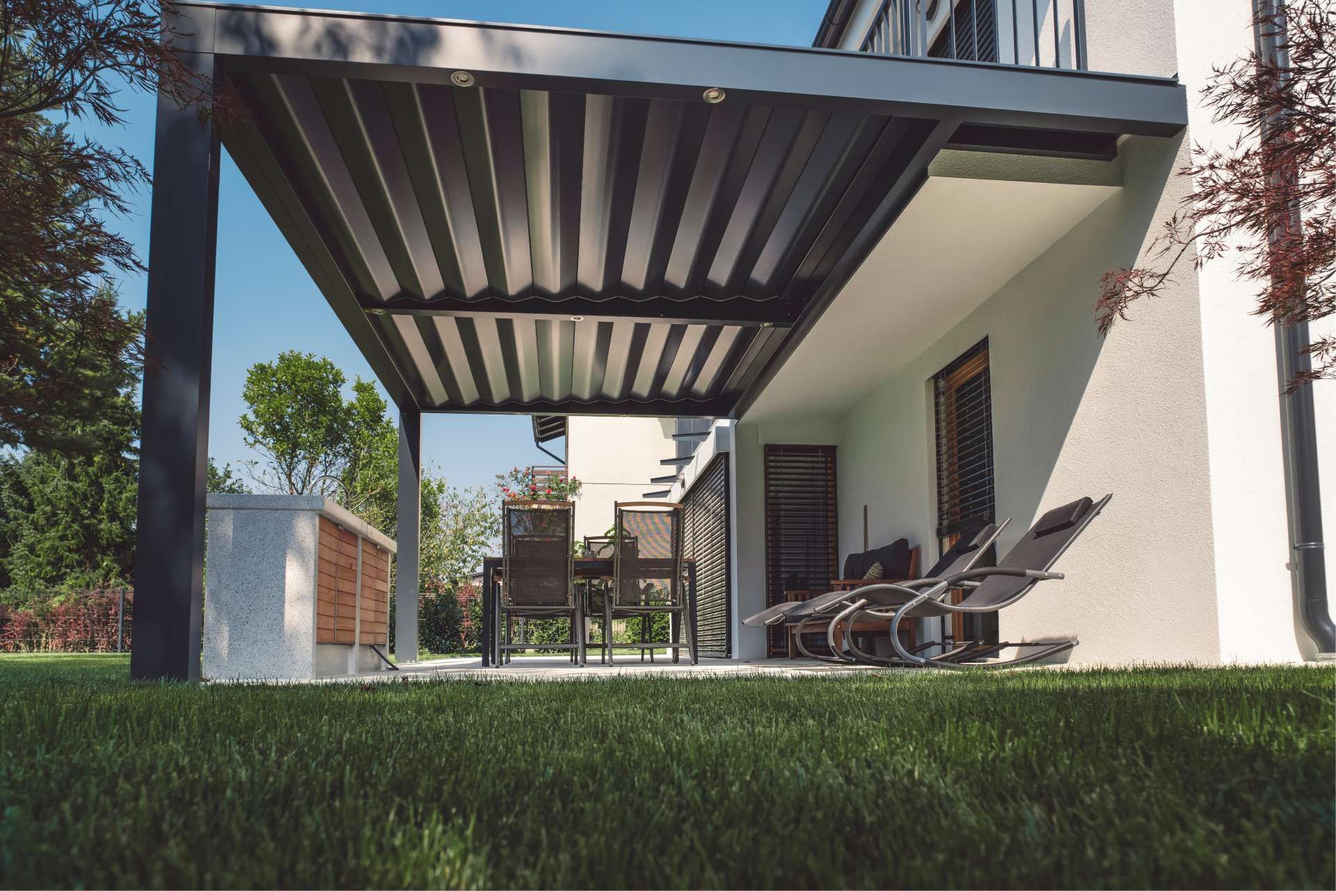 Modern pergola shades a patio with furniture and lawn in the foreground.