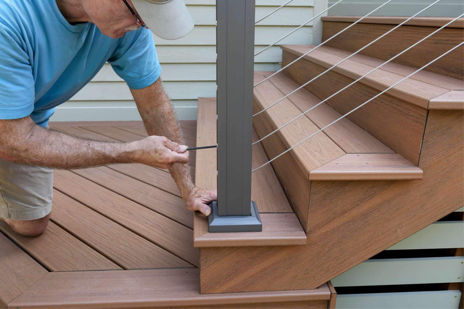 Man installing a cable railing on outdoor stairs; using a screwdriver. Composite decking and post.