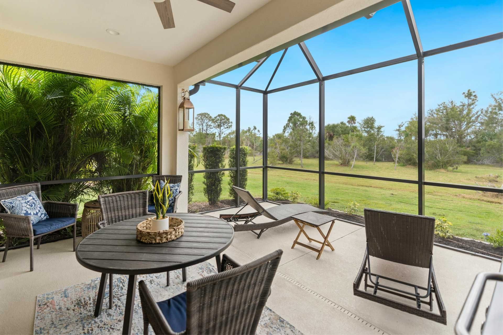 Screened-in patio with outdoor furniture overlooking a grassy field under a blue sky.