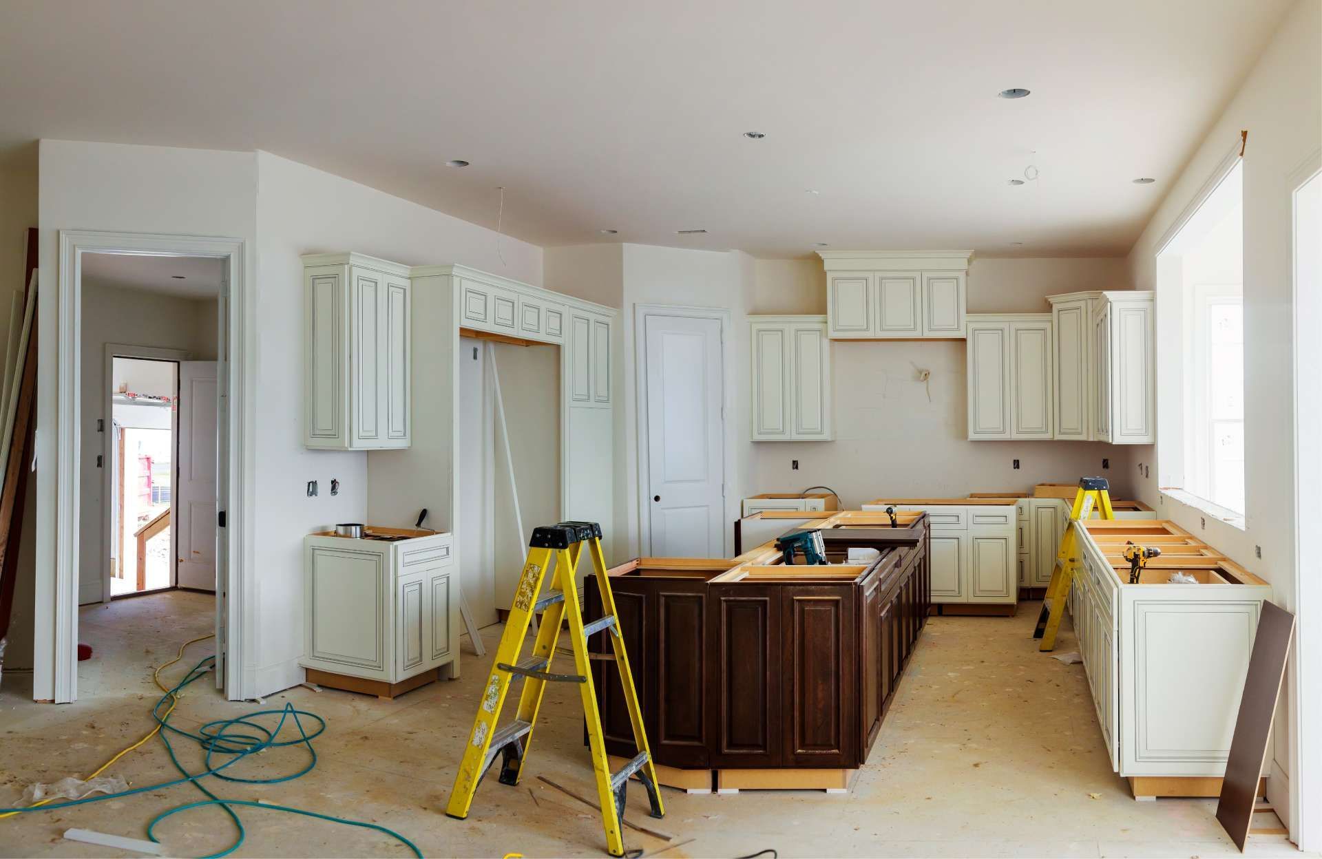 Kitchen under construction with unfinished white and brown cabinets, ladder, and exposed wires.