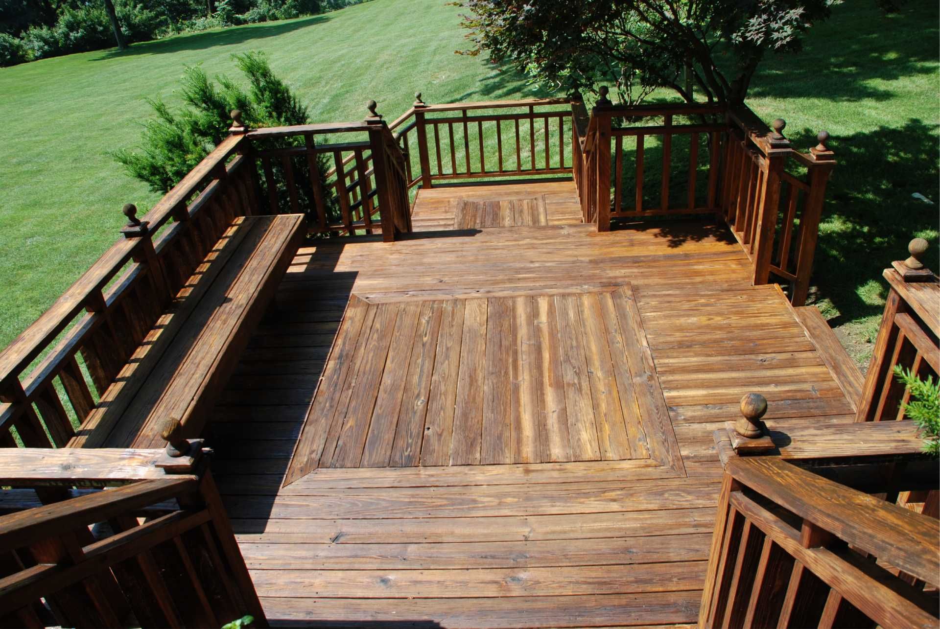 Wooden deck with built-in bench and railing, overlooking a green lawn.