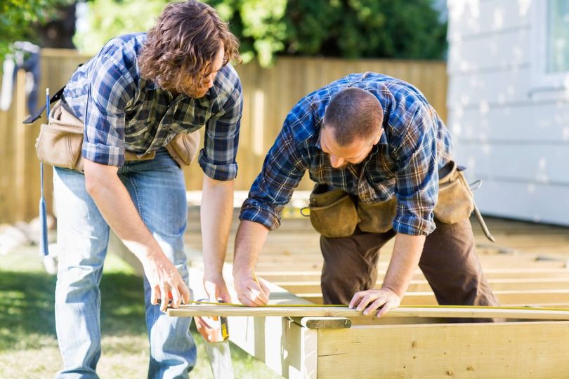 Two people in plaid shirts building a wooden deck outdoors.