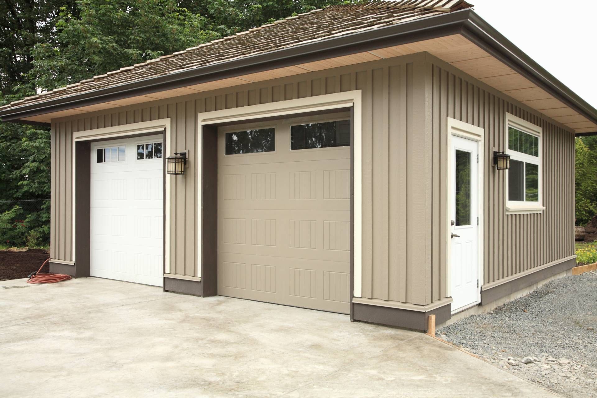 Tan and white two-car garage with vertical siding, brown trim, and a small white door.