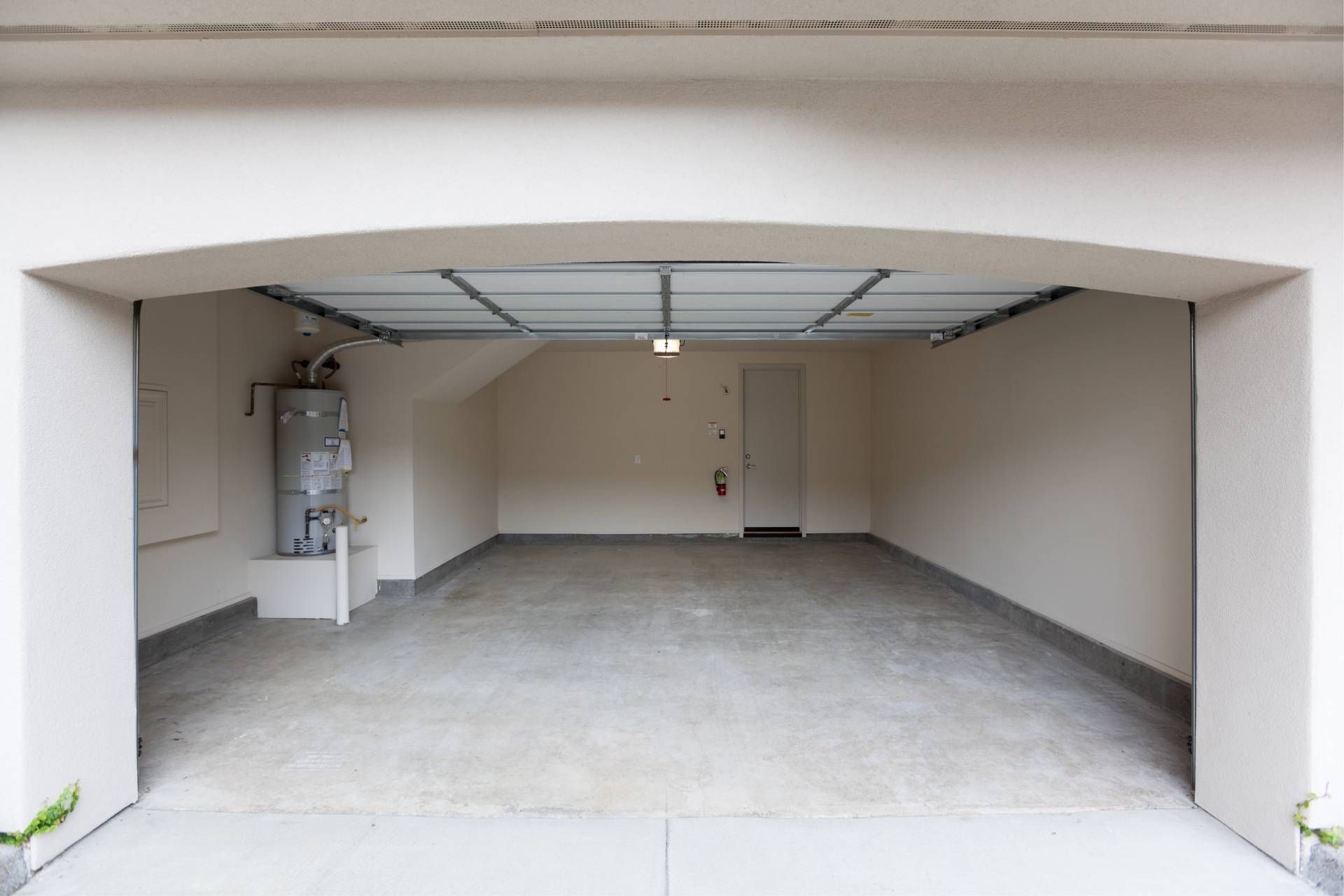 Empty garage with a concrete floor, a water heater, and a door.