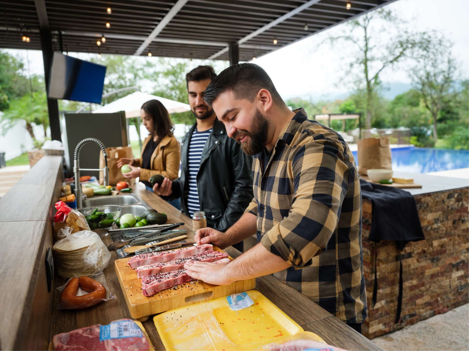 People preparing food outdoors; one man cutting meat, others nearby; sunny day.
