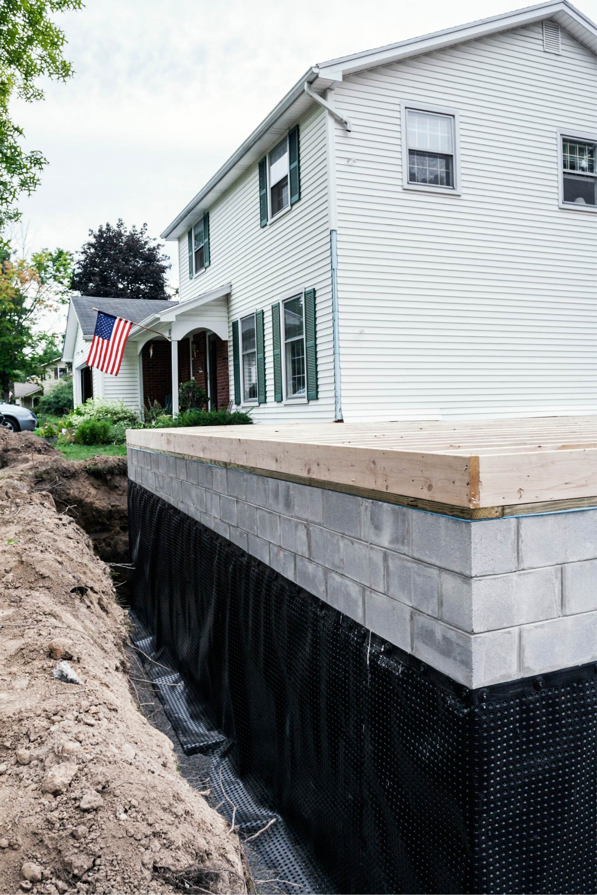 House with exposed cinder block foundation under construction, black waterproofing layer visible.