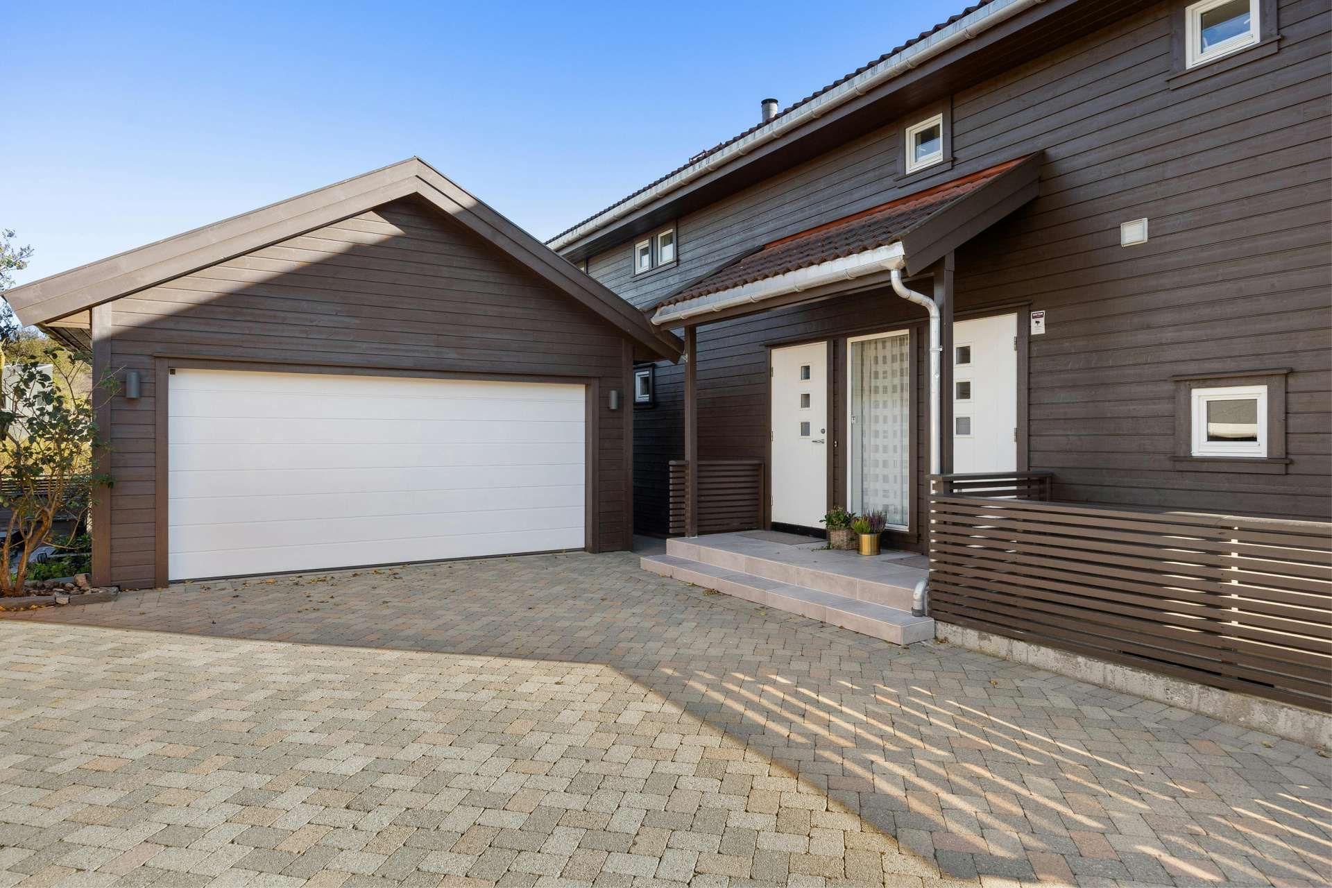 Brown house with white garage door and paved driveway.