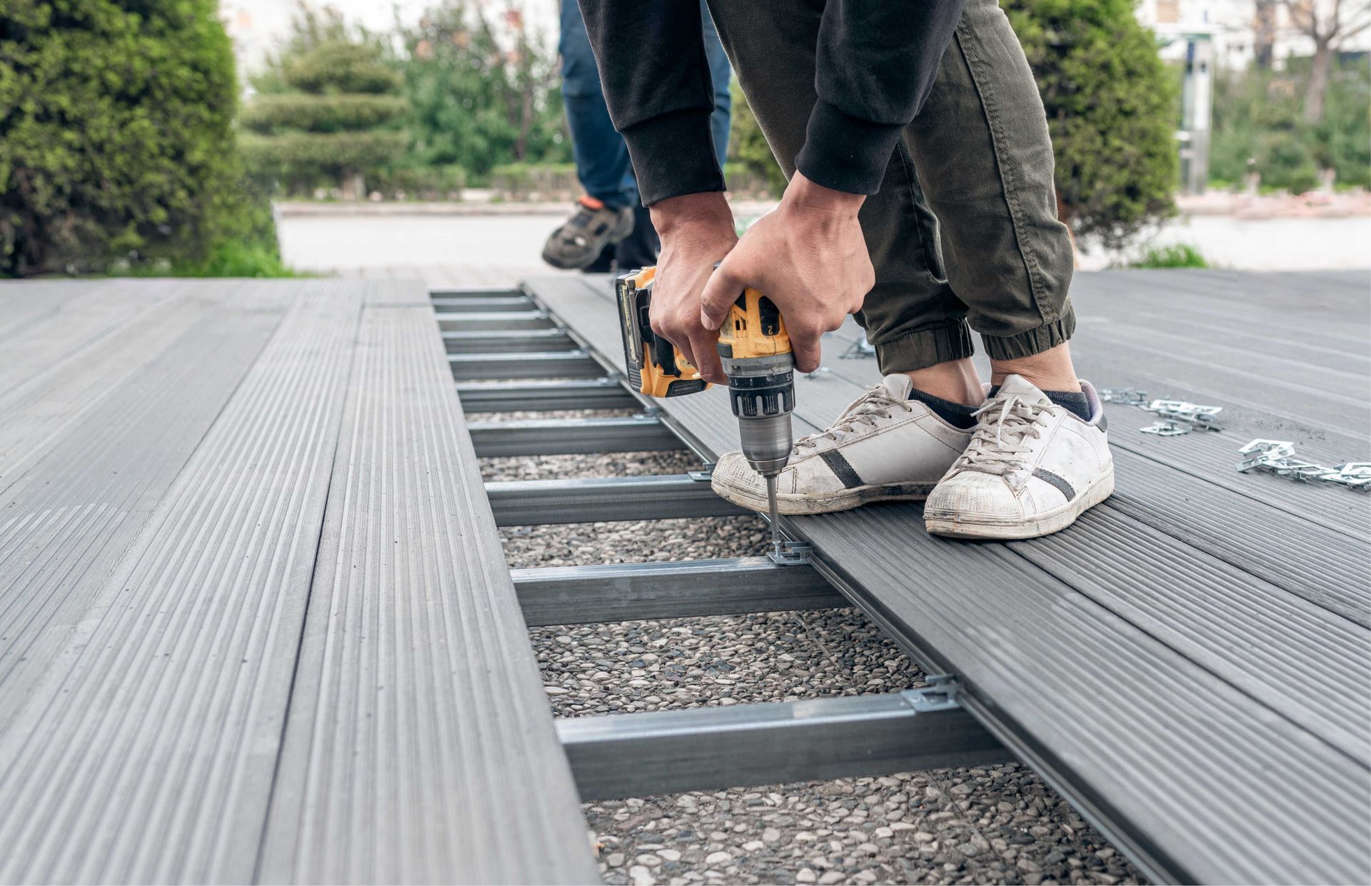 Person using a power drill to screw composite decking boards to a metal frame. Outdoors.