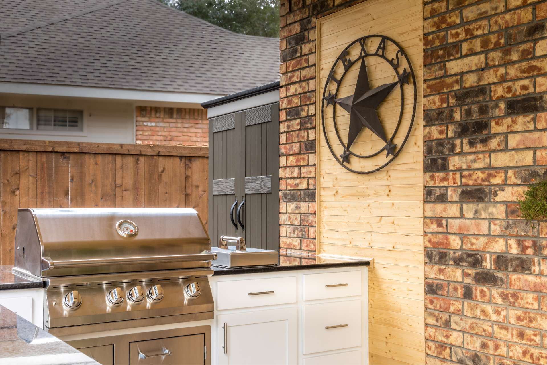 Outdoor kitchen with stainless steel grill, white cabinets, brick wall with Texas star decor.