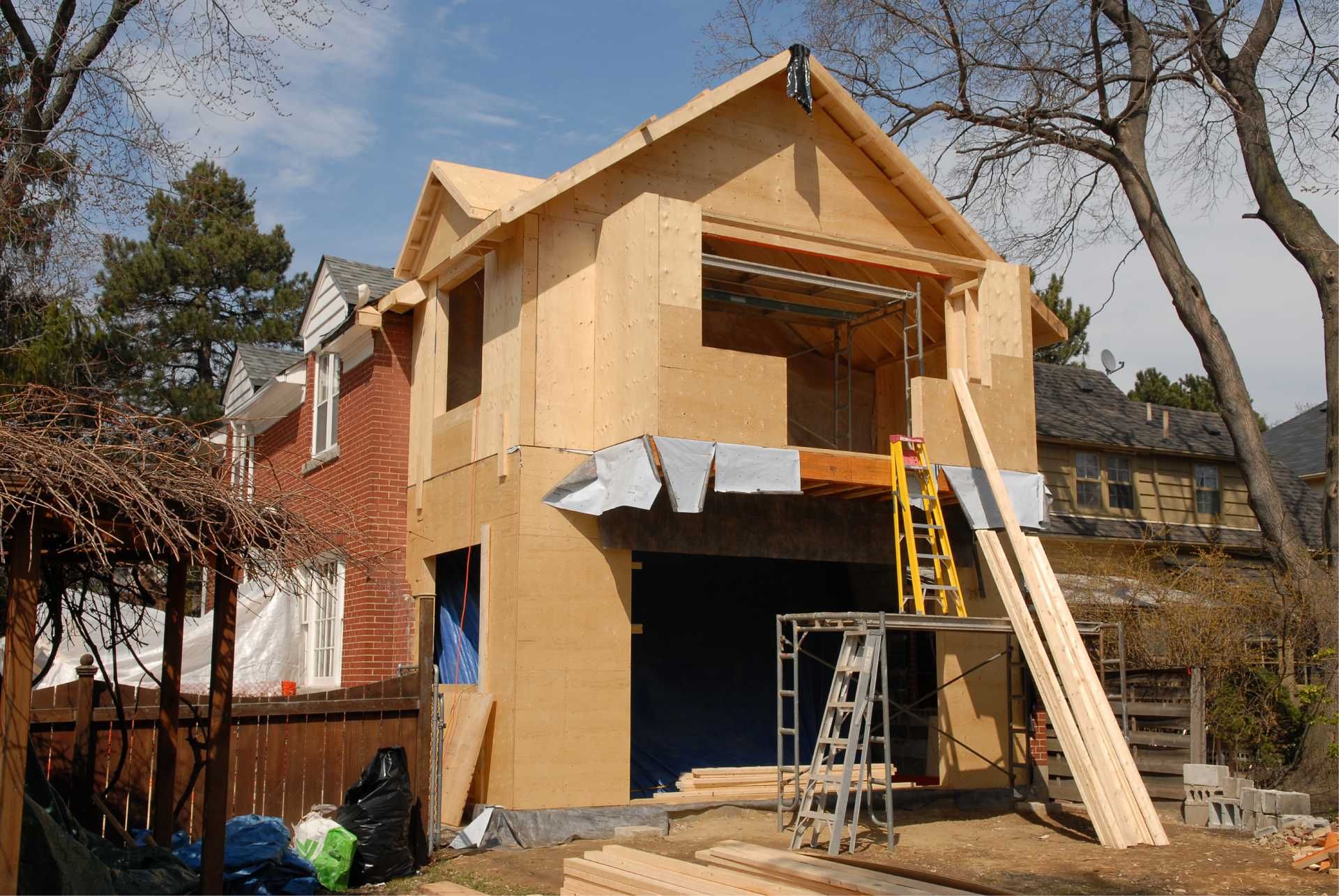 Construction of a two-story wooden addition to a brick house. Ladder and lumber present.