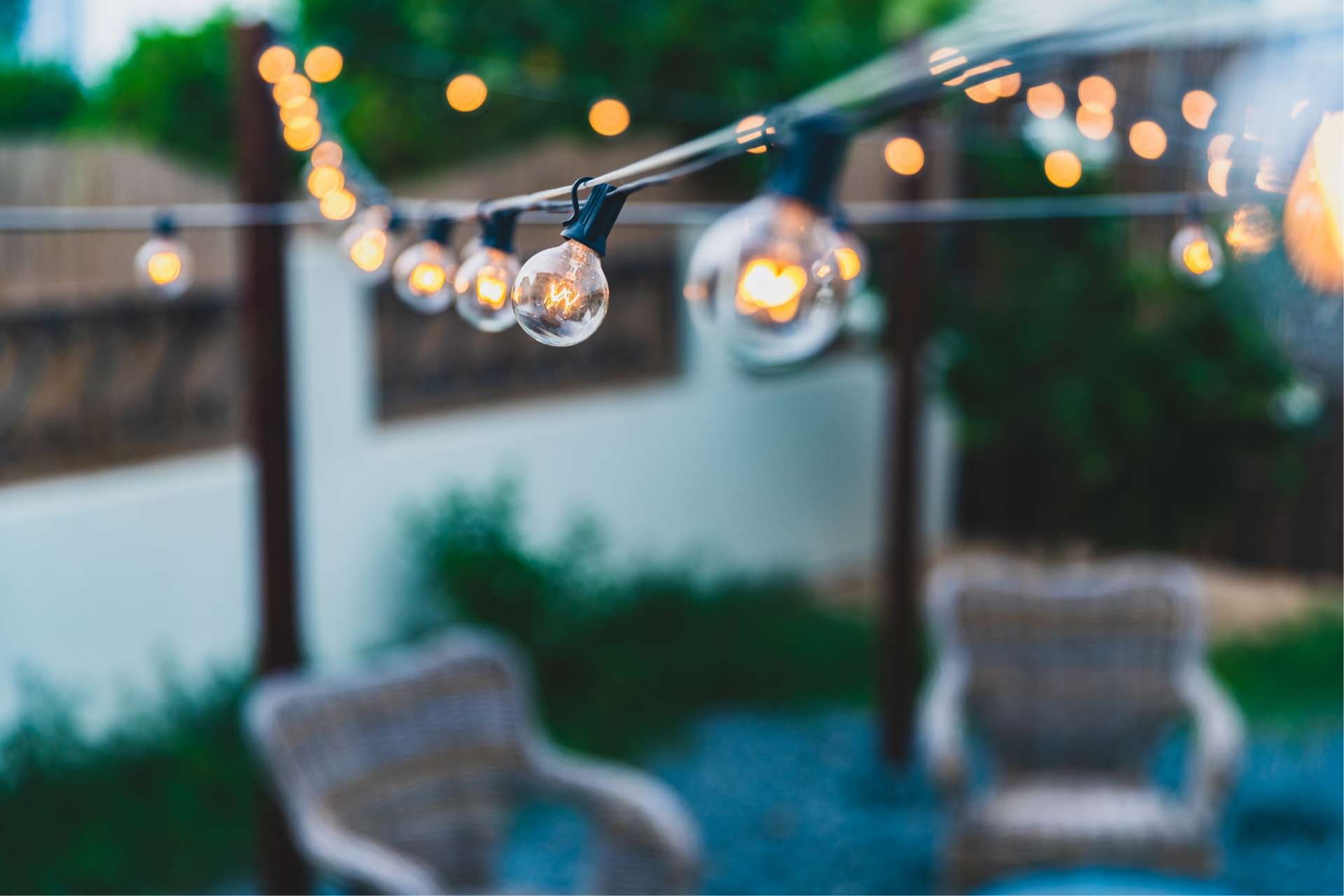 String lights illuminate a backyard patio with wicker chairs.