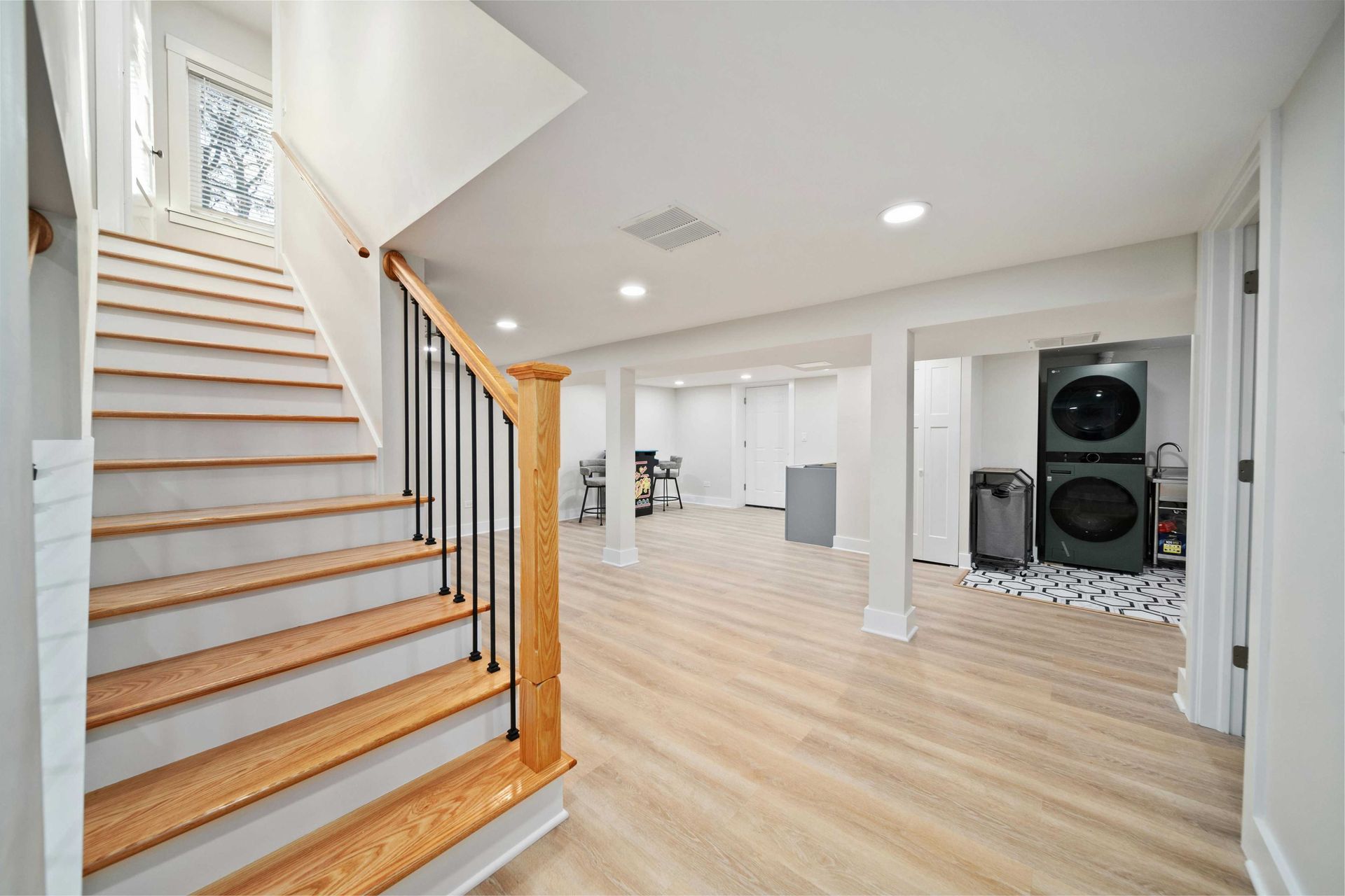 Basement interior with stairs, light wood floor, white walls, and a washer/dryer unit.