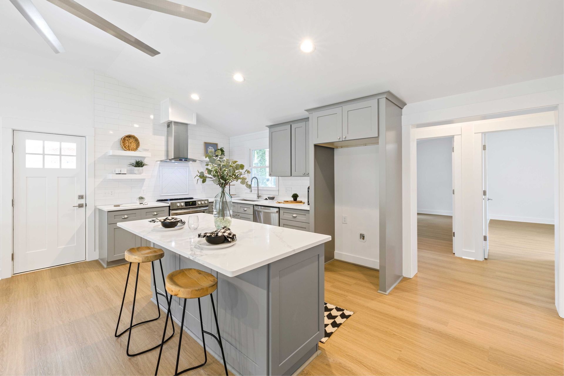 Modern kitchen with gray cabinets, white countertops, and wood flooring; island with stools.
