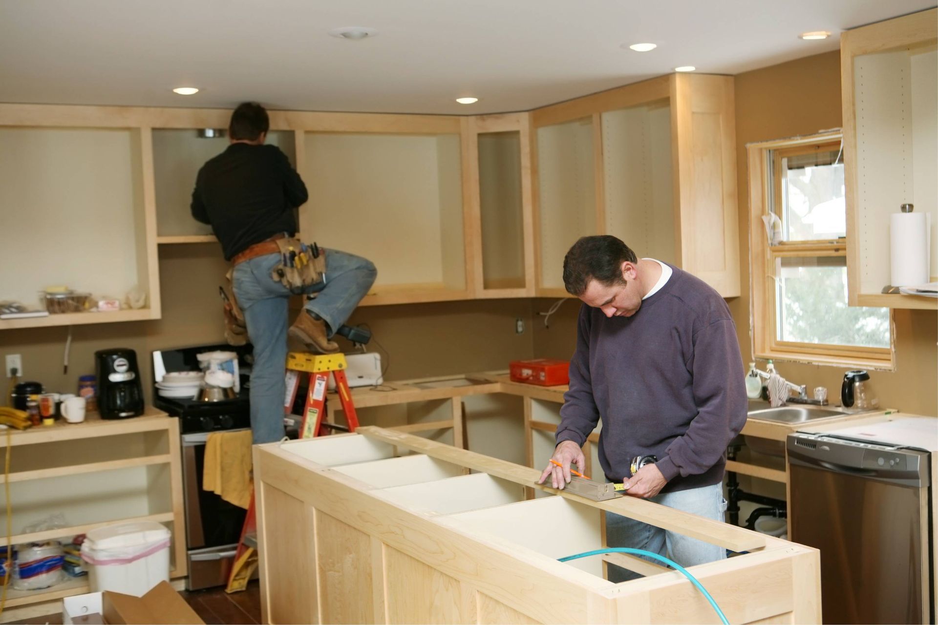 Two people installing kitchen cabinets; one on a step ladder, another at the counter.