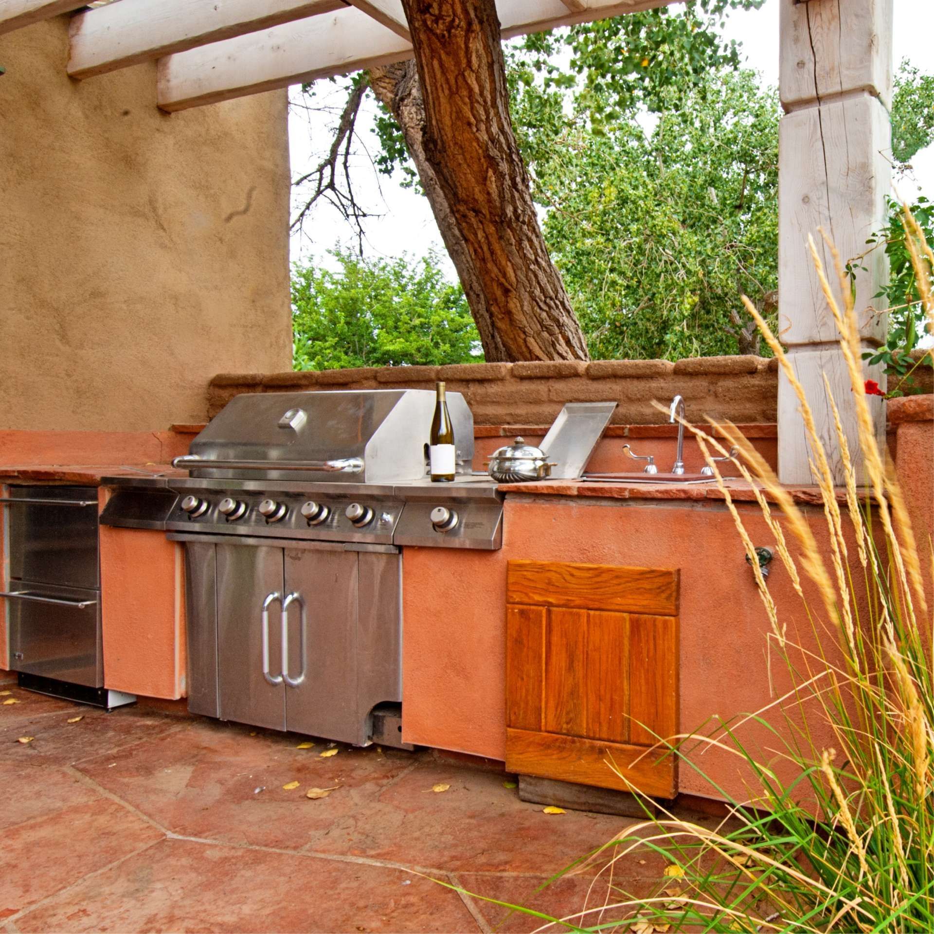 Outdoor kitchen with stainless steel grill, red stucco, and tree growing through the structure.