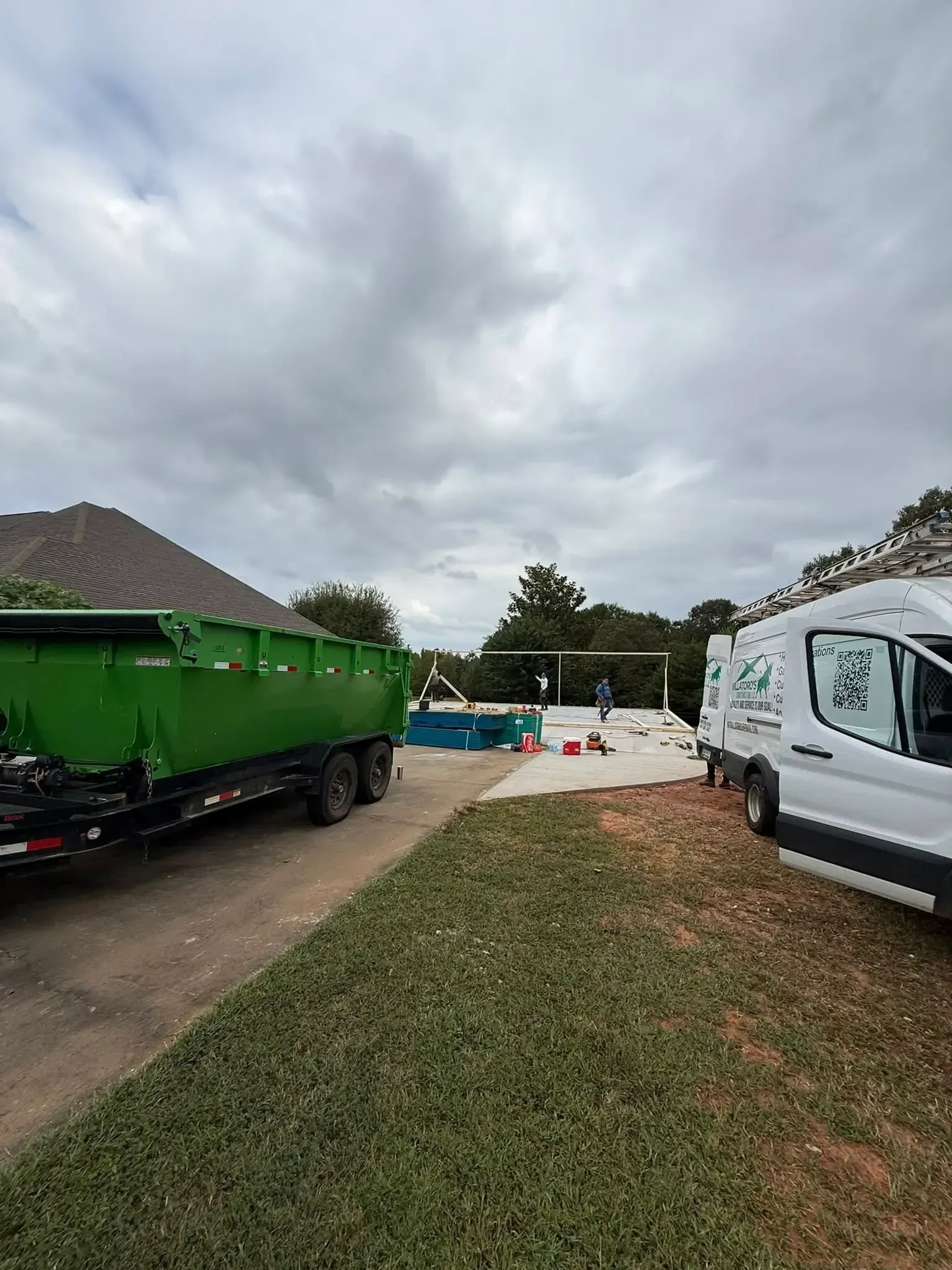 Gray house with detached garage; dirt driveway, green grass, blue sky.