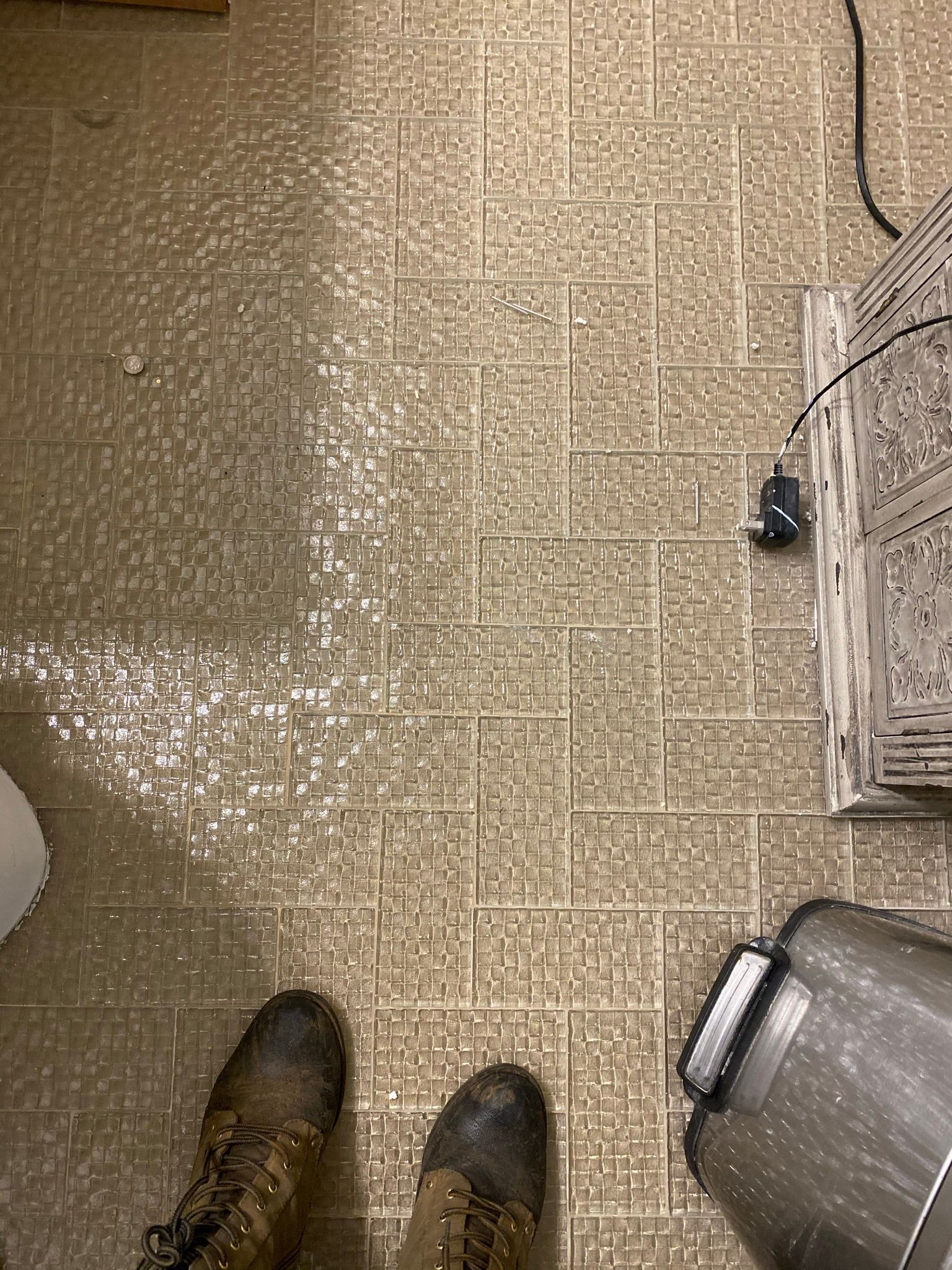 A person is standing on a tiled floor next to a trash can.
