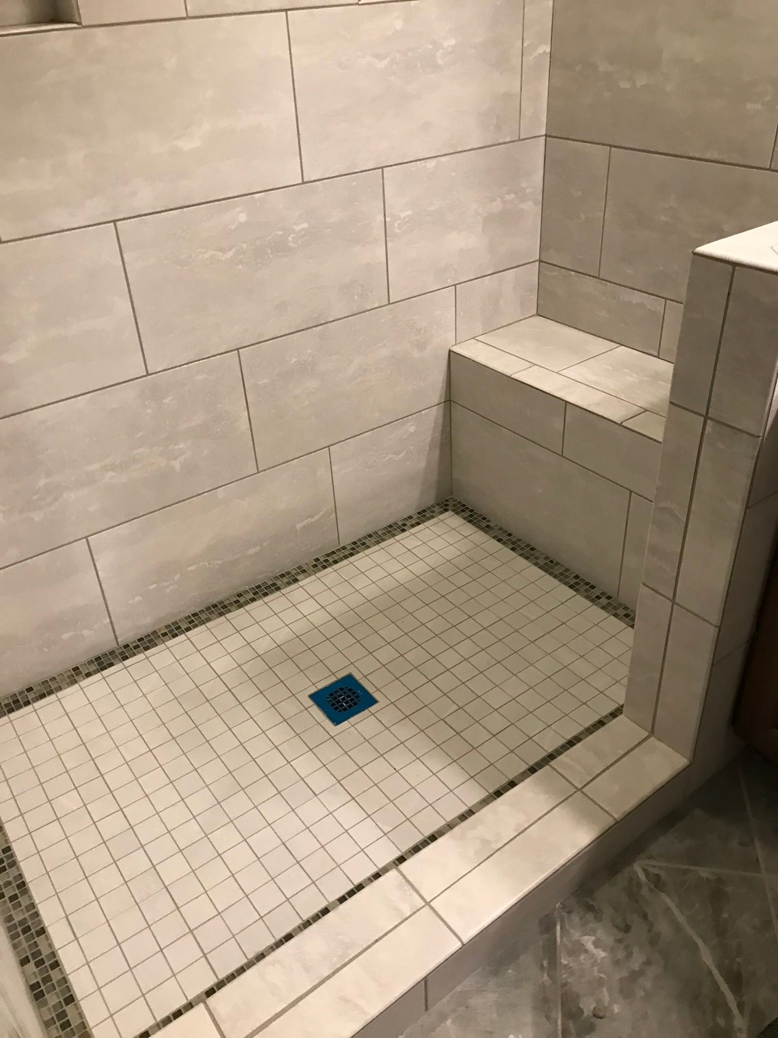 A shower stall with white tiles and a blue drain