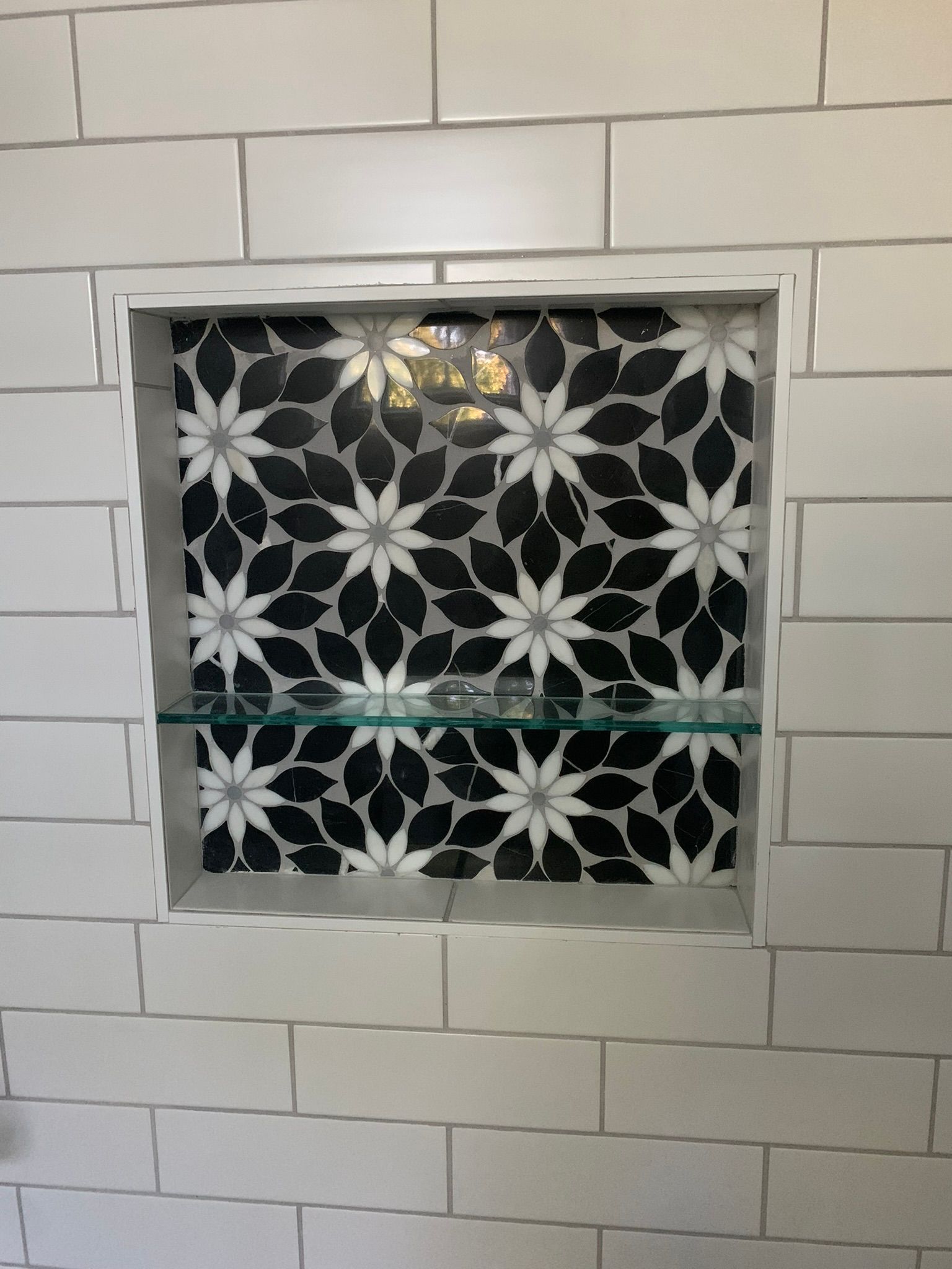 A black and white tile shower niche with a glass shelf