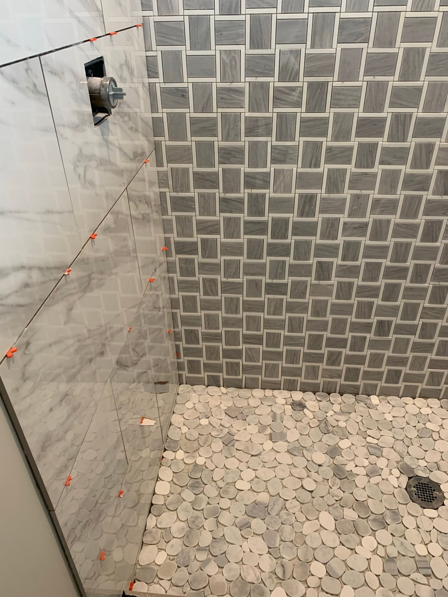 A shower with a gray tile wall and a white tile floor