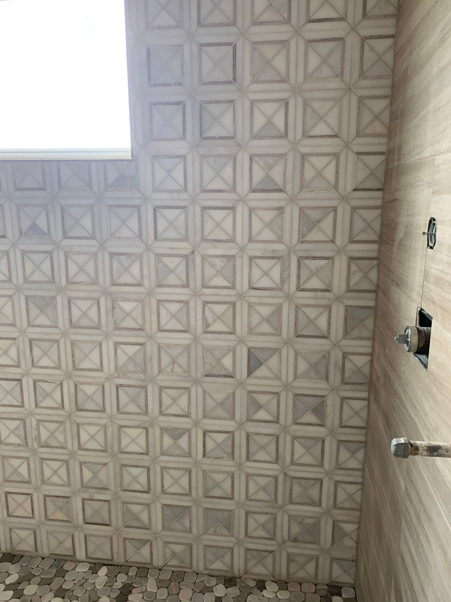 A shower with a tiled wall and a window.