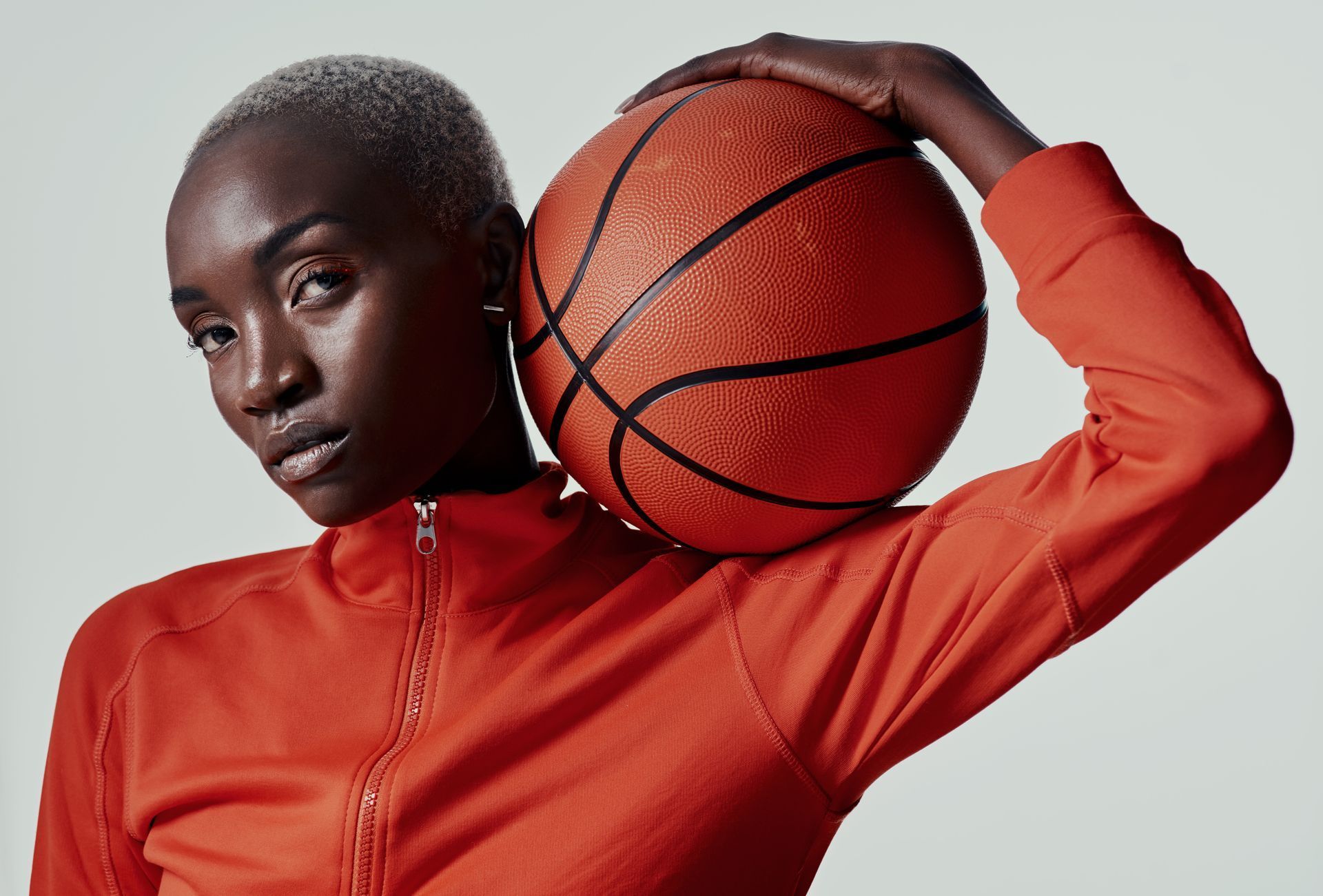 Woman with shaved head in orange shirt holds a basketball.