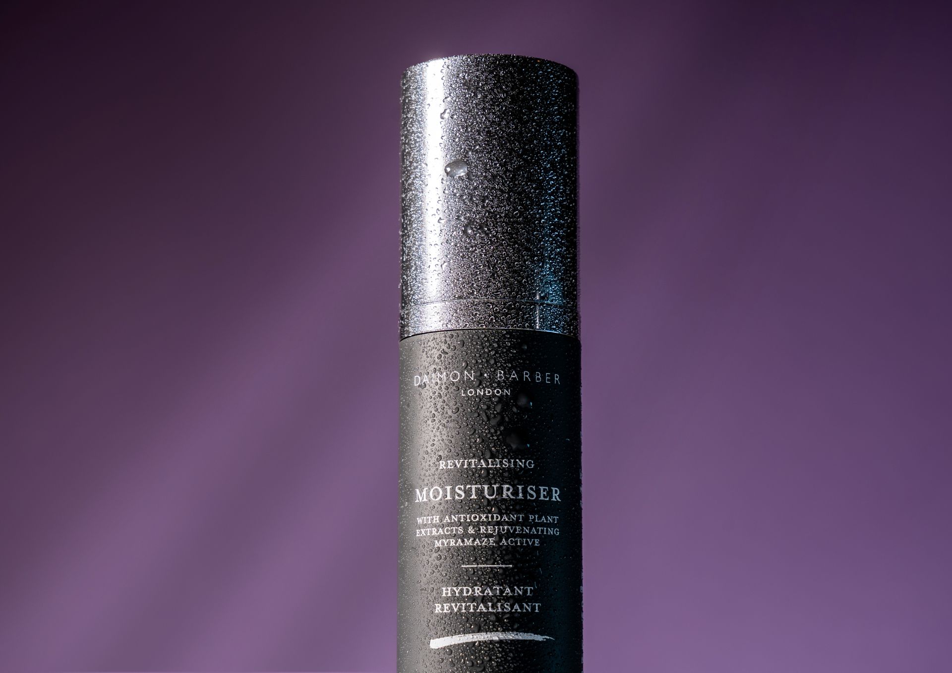 A black bottle of moisturizer is sitting on a purple surface.