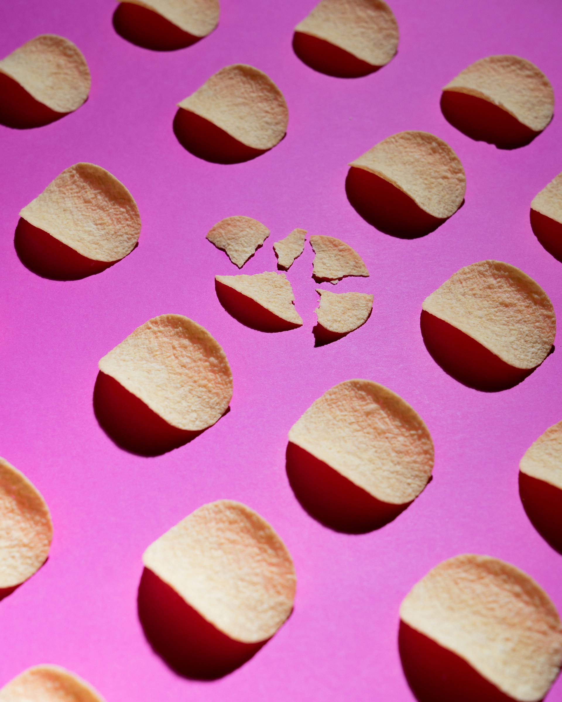 A row of potato chips on a pink surface with one broken in half