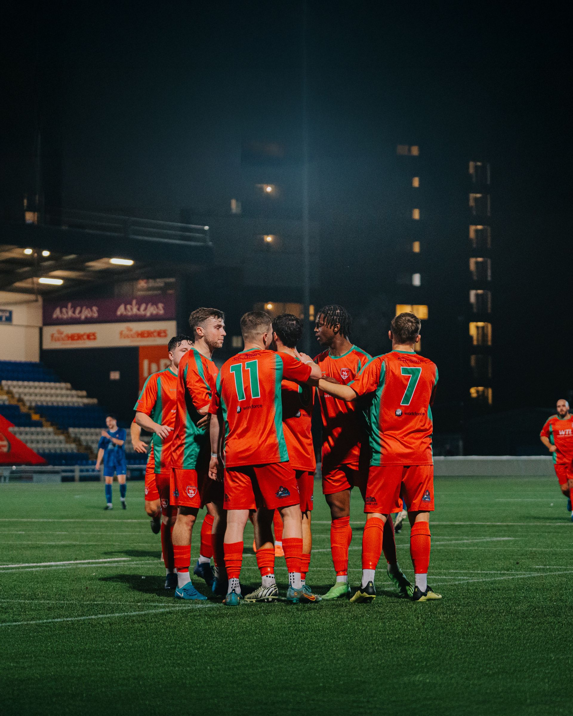 A group of football players are standing in a huddle on a field at night.