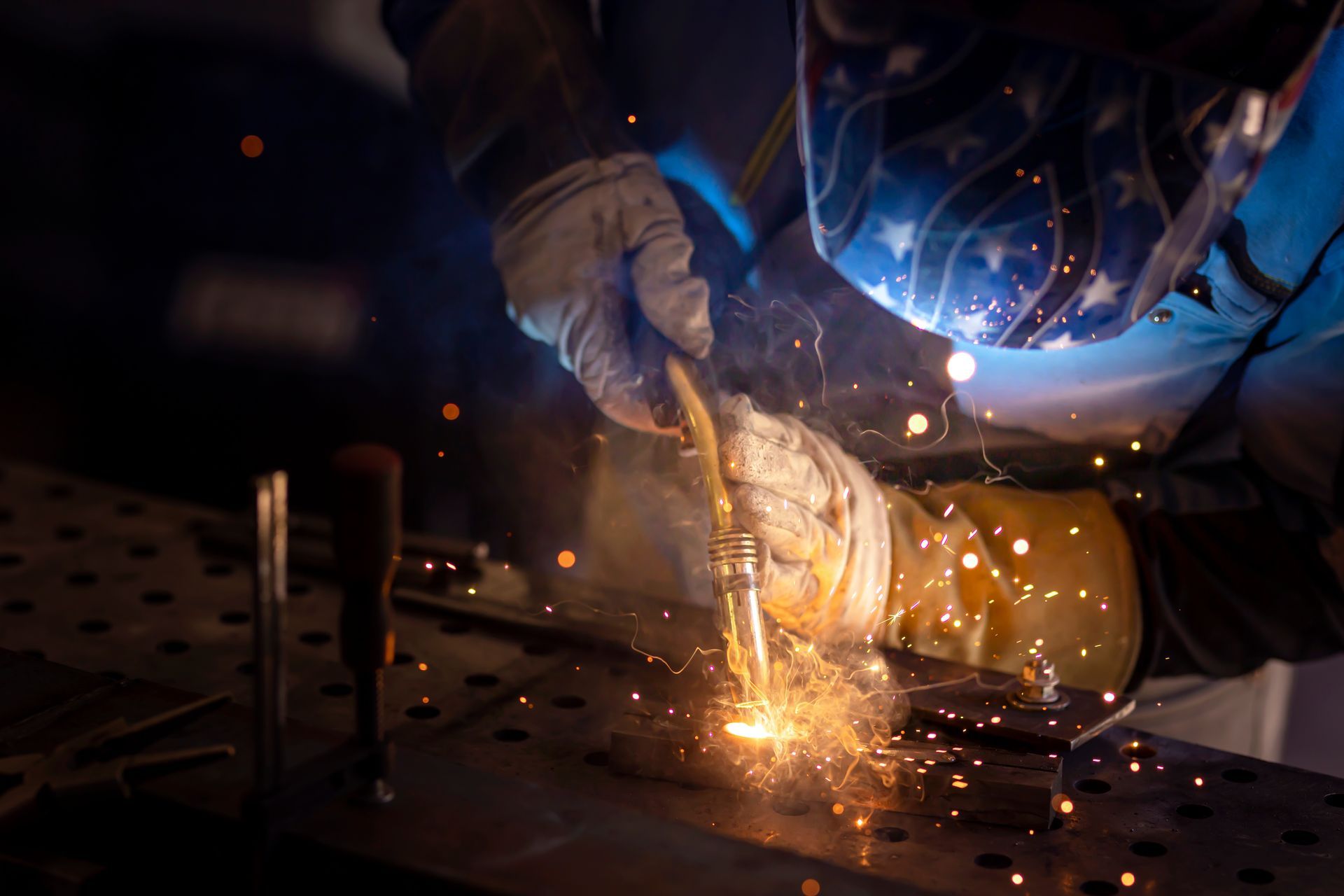 Welder using a torch, creating sparks on metal in a dim setting.