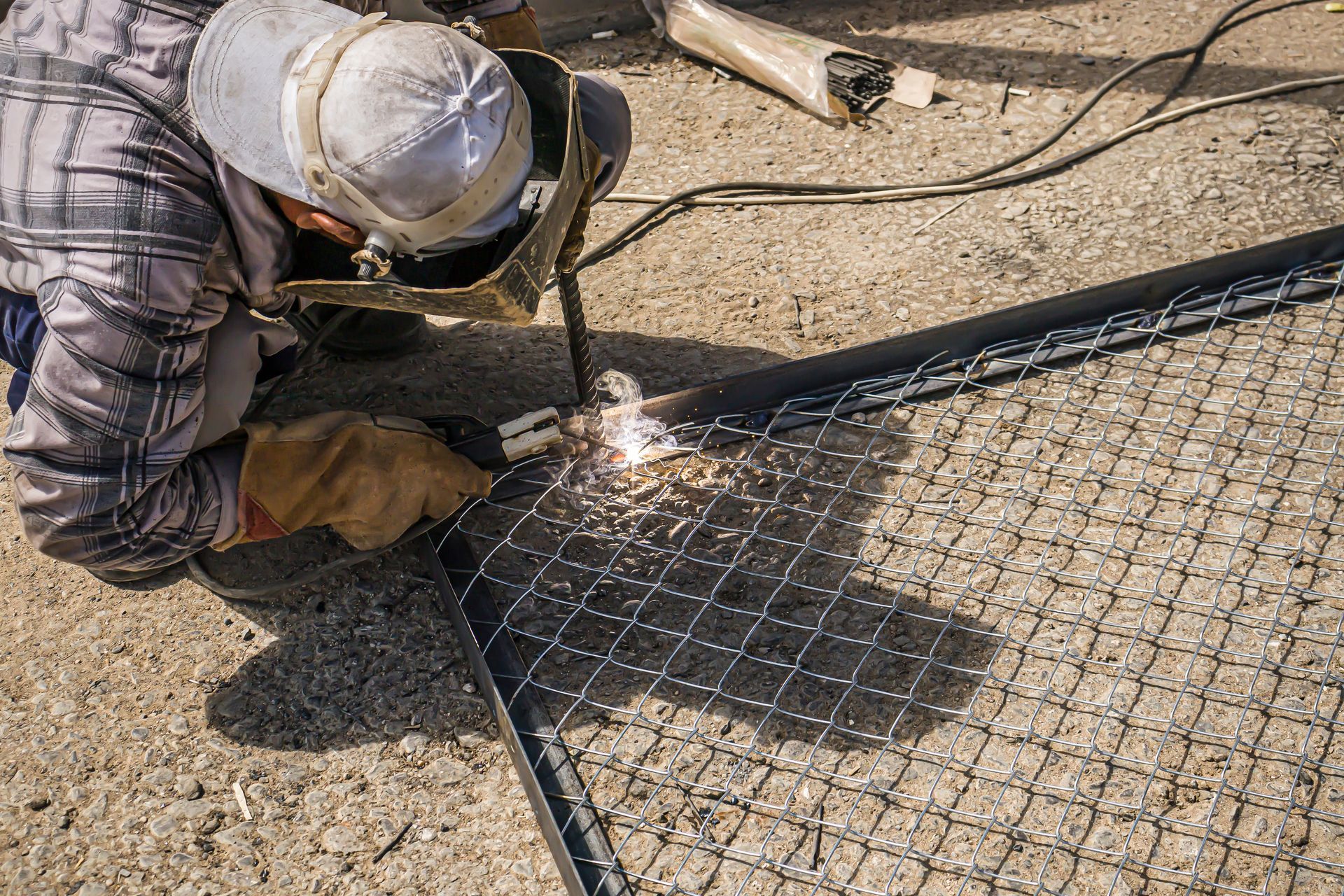 Person welding metal fence, sparks flying, outdoors.
