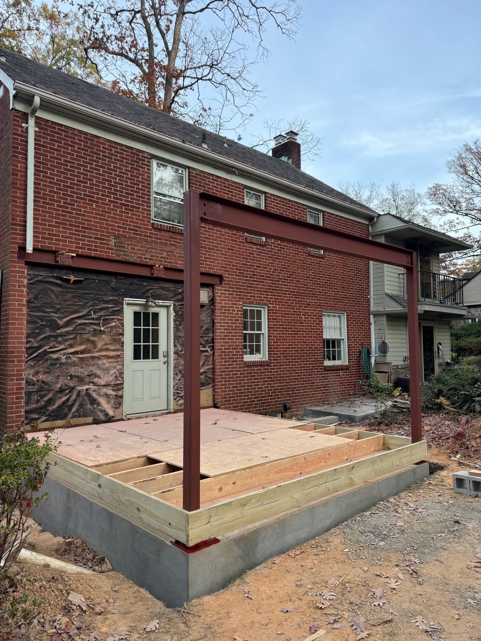Construction of a patio with a metal frame and brick house backdrop.