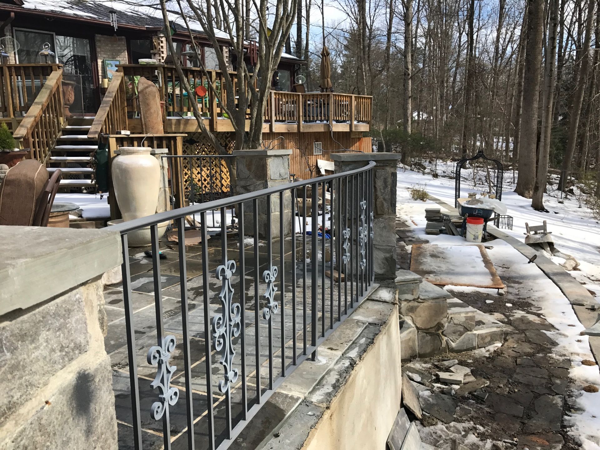 Stone patio with wrought iron railing; house and snowy woods in background.