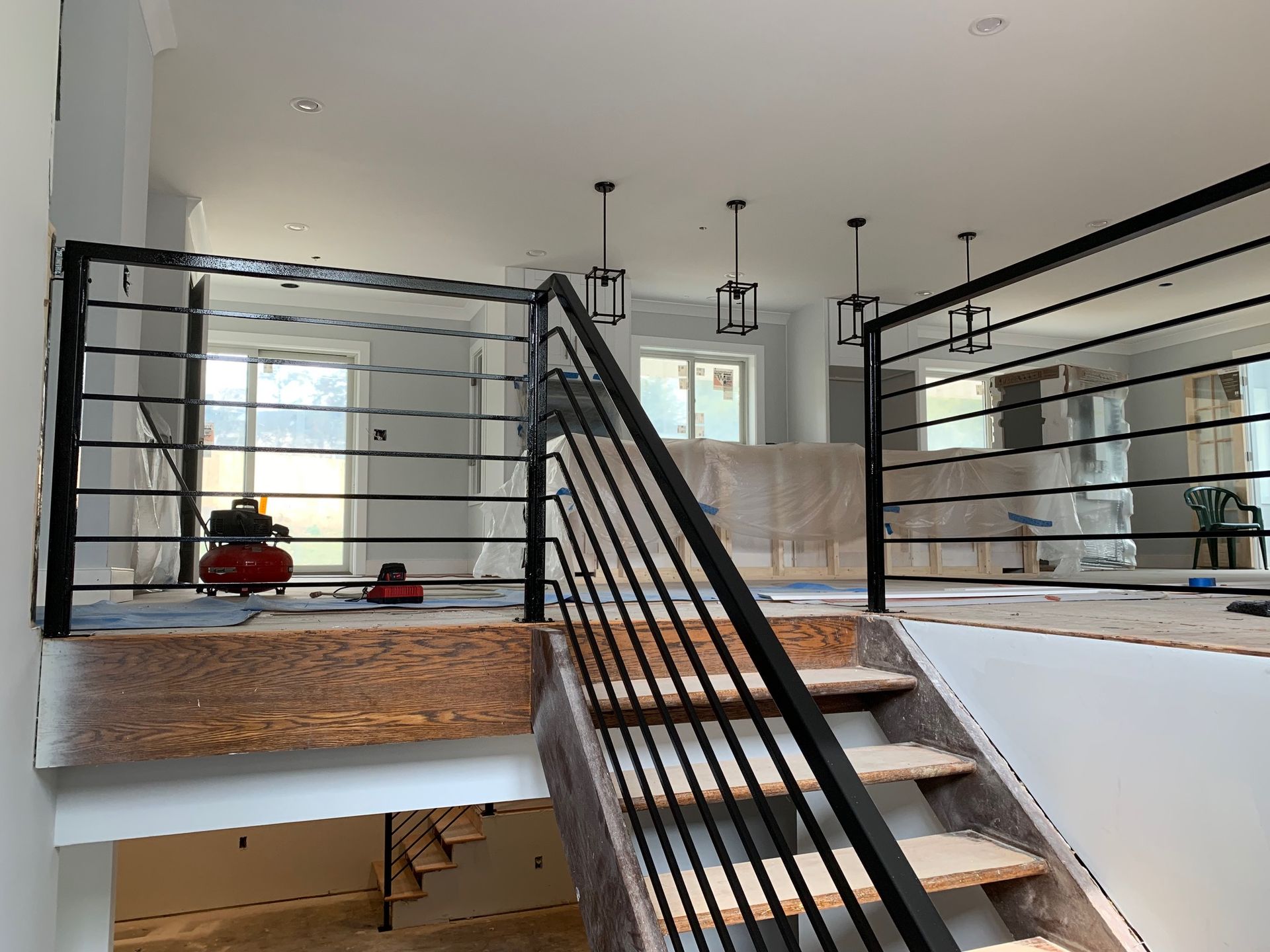 Interior view of a staircase with black metal railing, open to a second story with windows and lights.