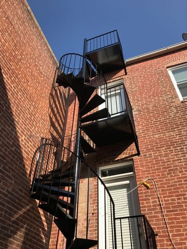 Black spiral staircase attached to a brick building.