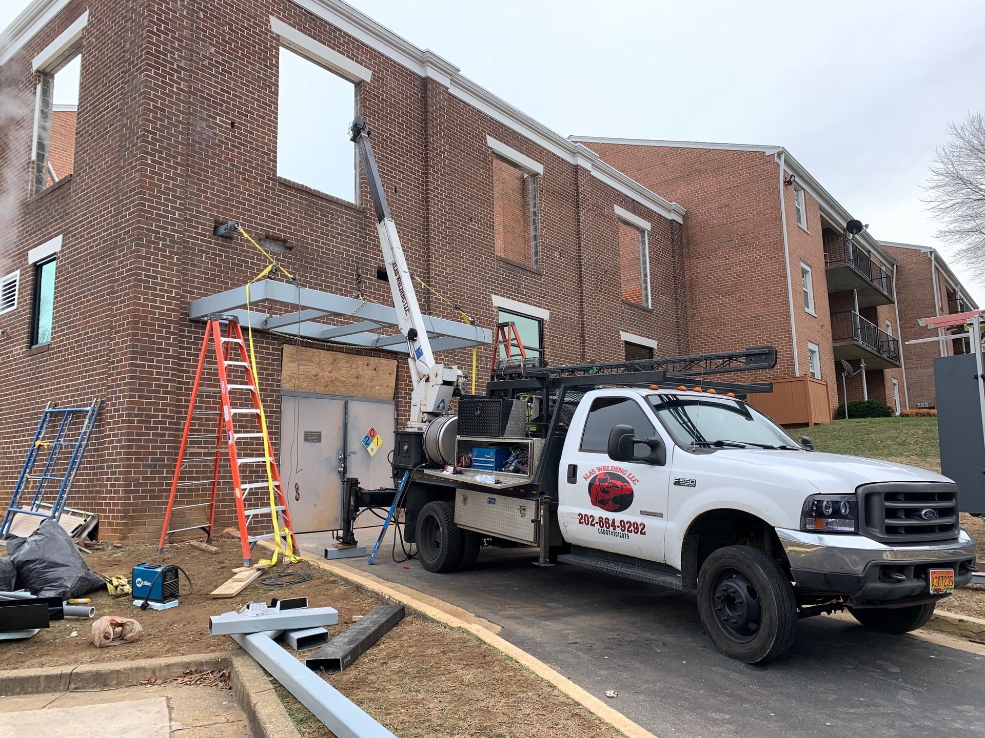 A white work truck with a crane is parked next to a brick building. Construction is in progress.