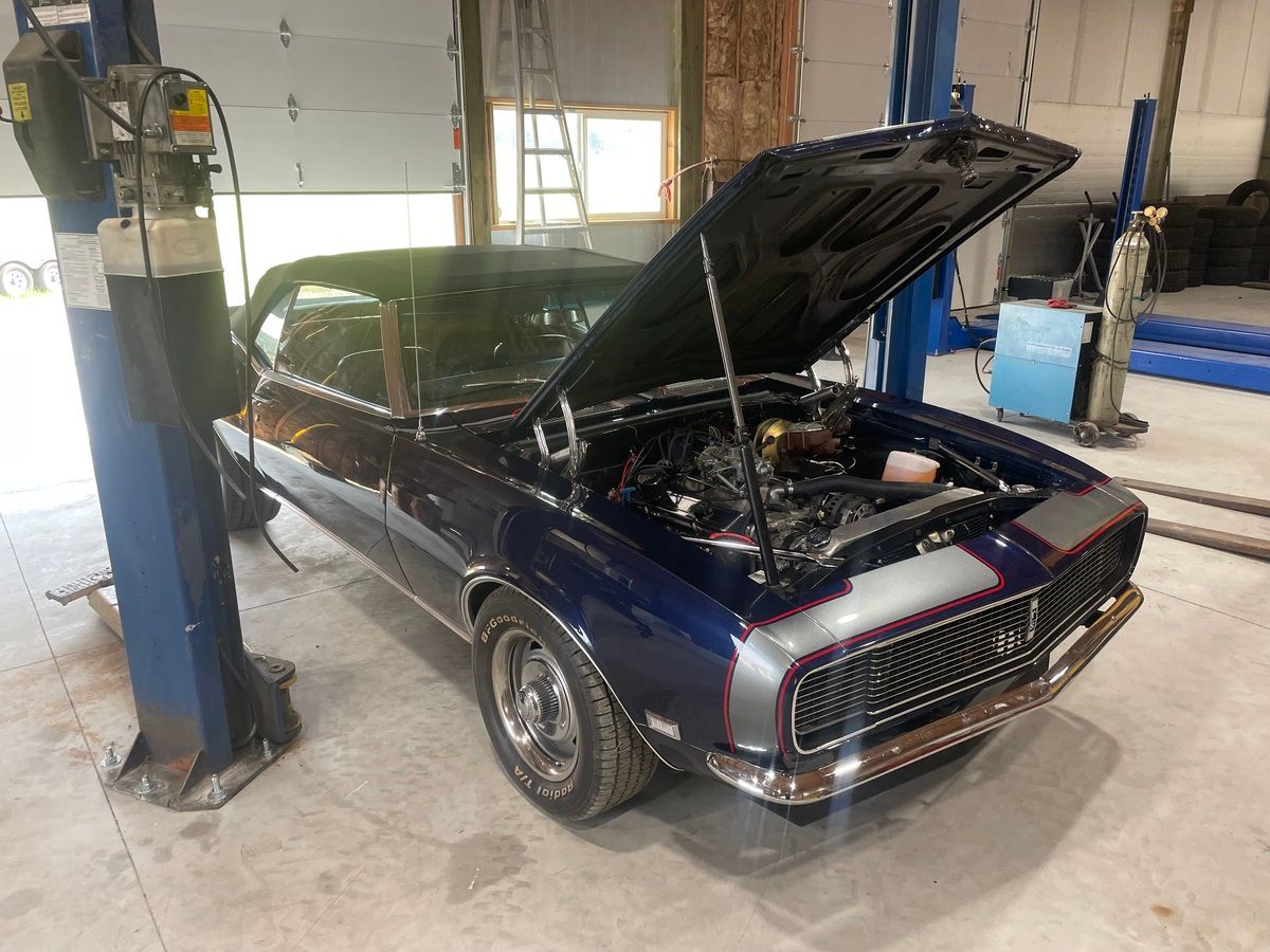 A blue car with the hood up is parked in a garage.